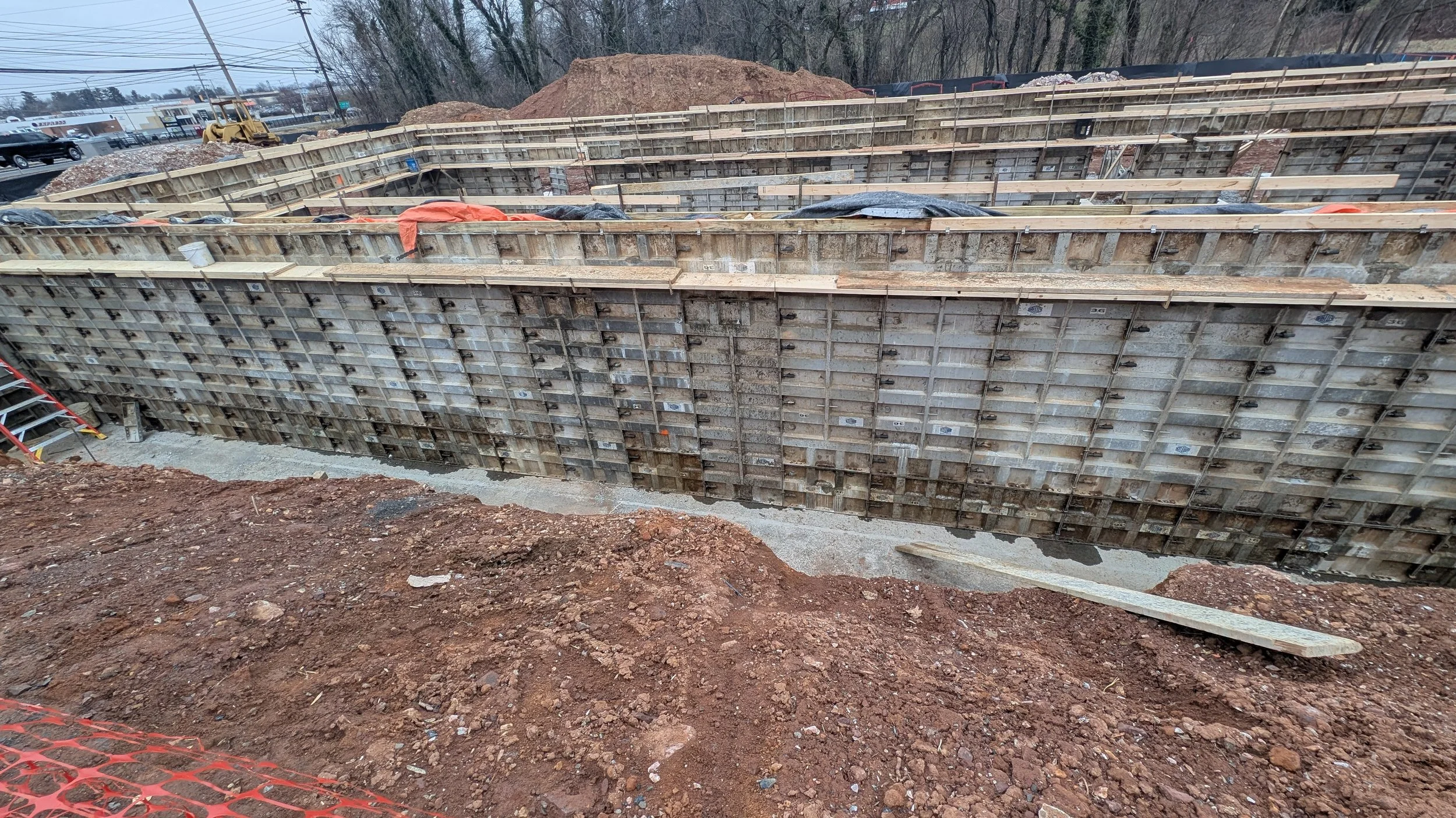 Construction site with excavation and formwork for a new structure, surrounded by dirt and construction equipment.