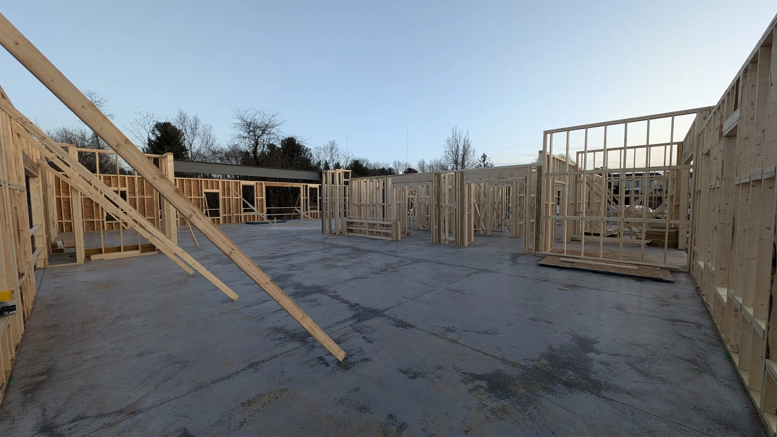Construction site with framed wooden walls and concrete floor, no roof or fixtures installed yet.