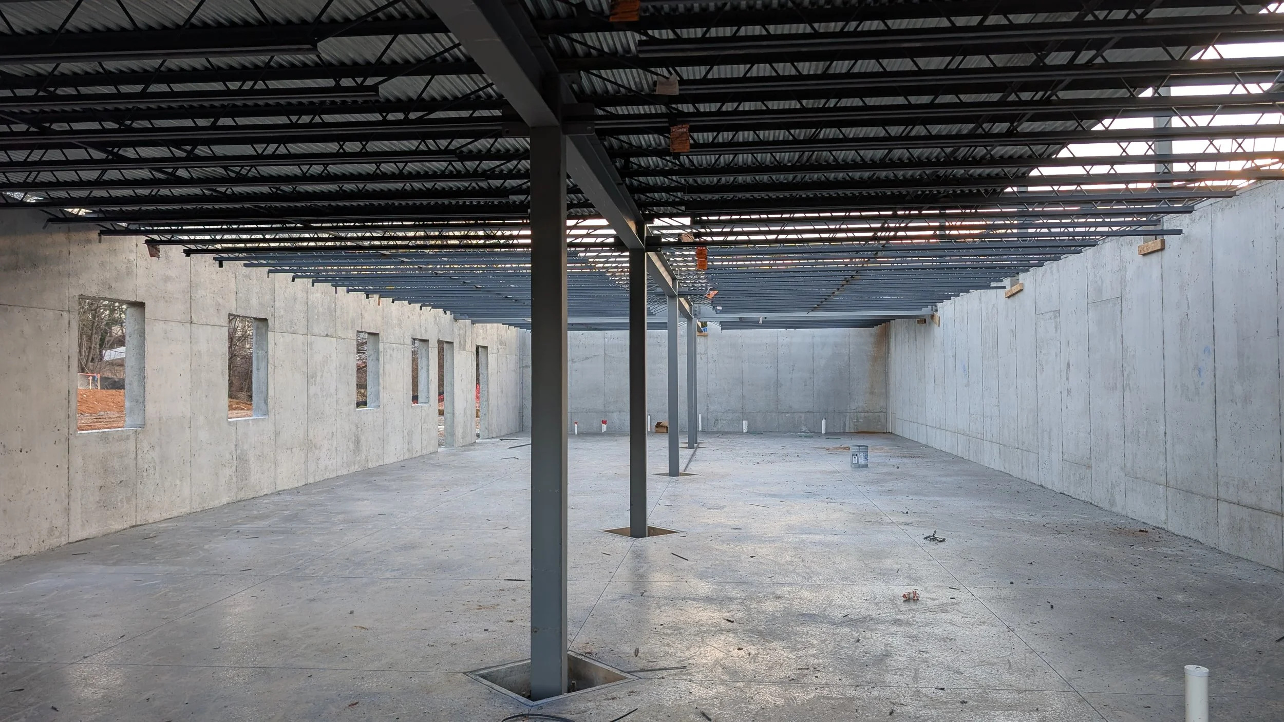 Interior of a building under construction with concrete walls, a concrete floor, and electrical and structural framing in place for the ceiling.