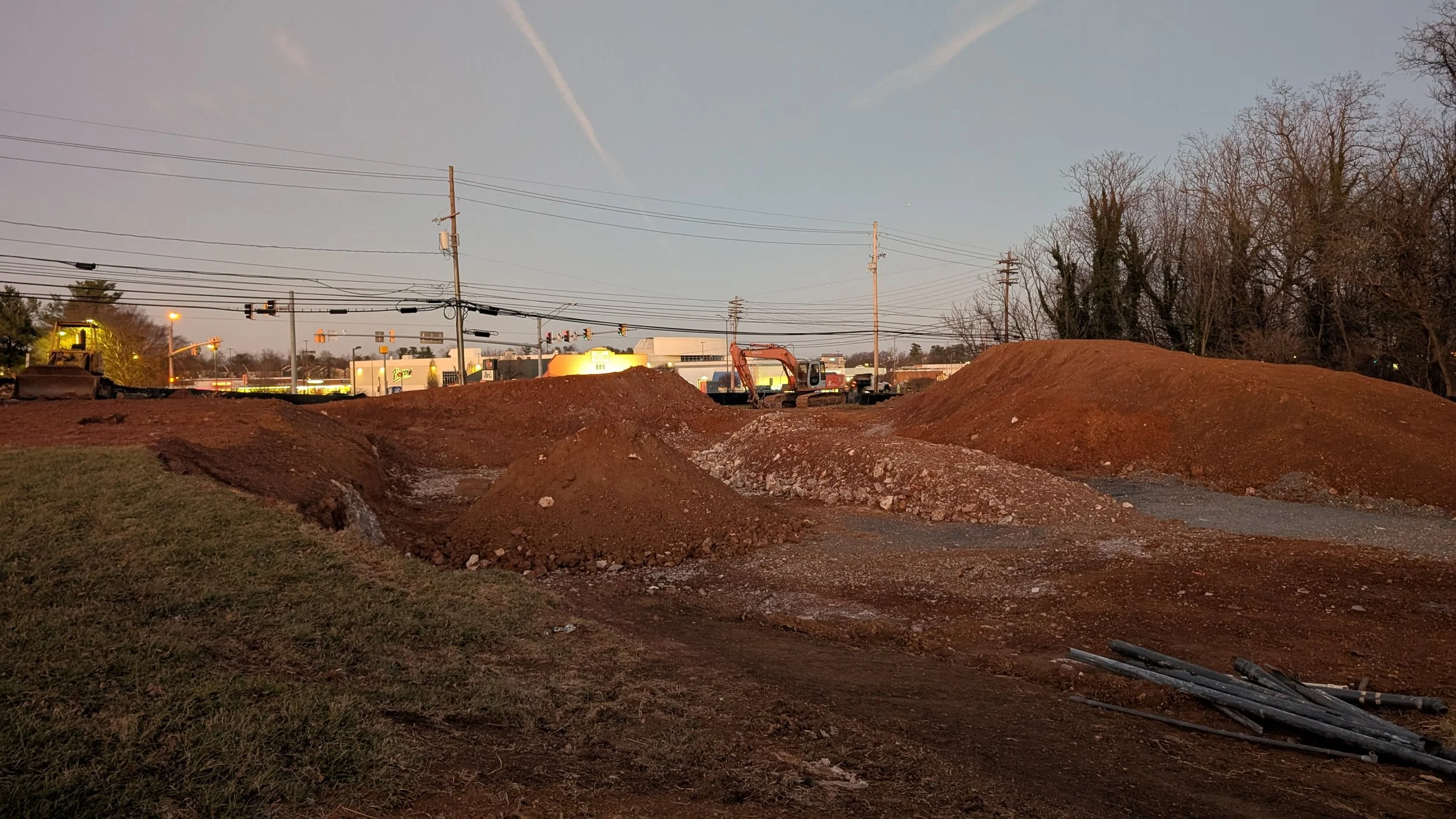 Construction site with dirt mounds, excavation equipment, and power lines at dusk