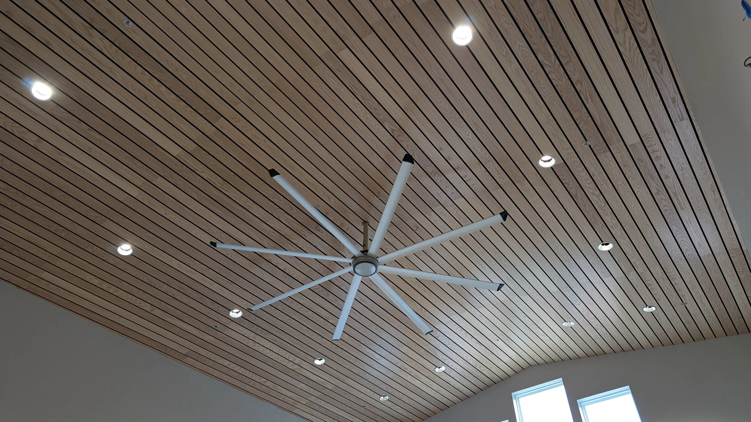 View of a wooden ceiling with a modern white ceiling fan and several recessed lights.