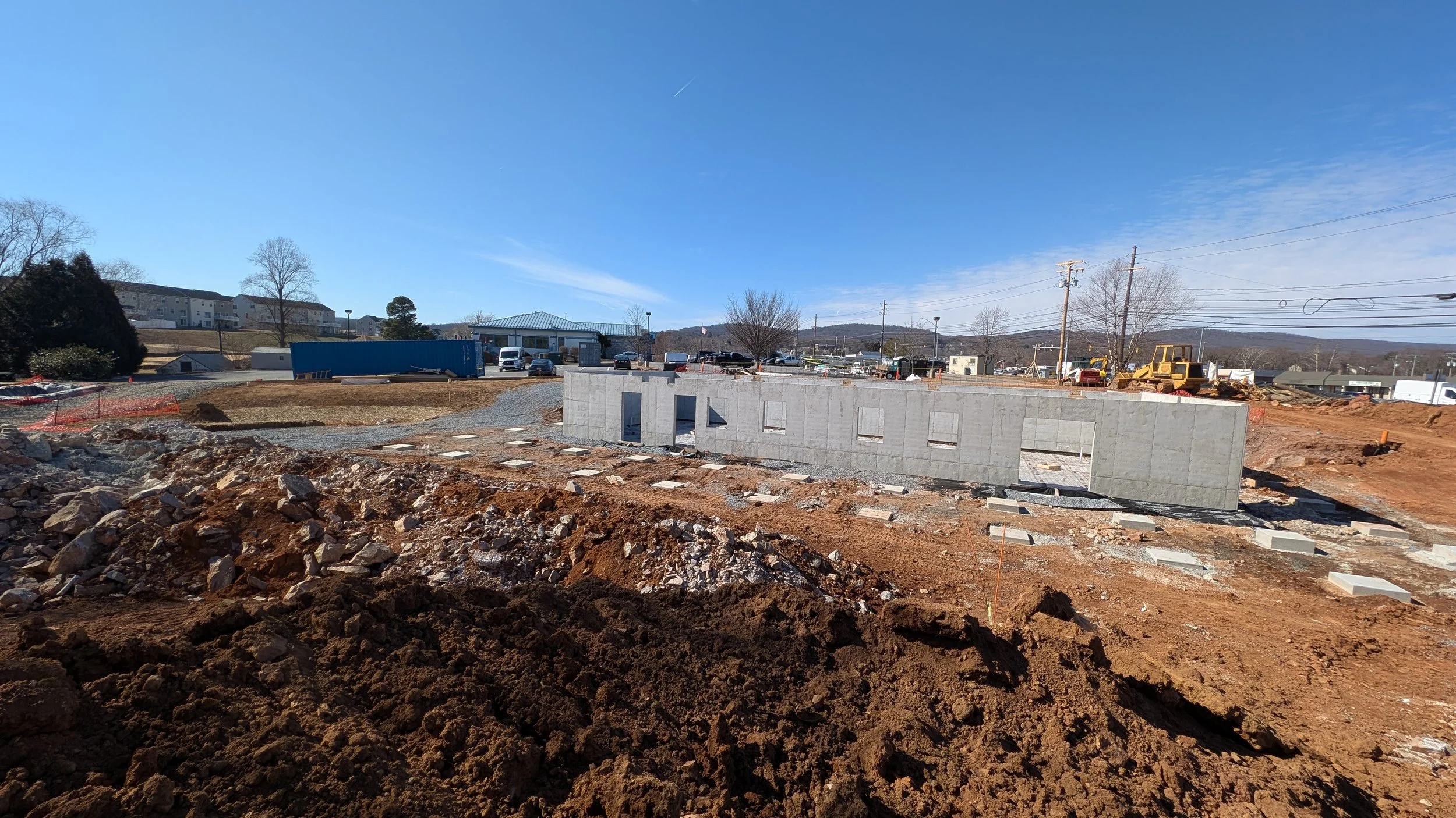Construction site with a partially built concrete wall, dirt., and construction equipment, under a clear blue sky.