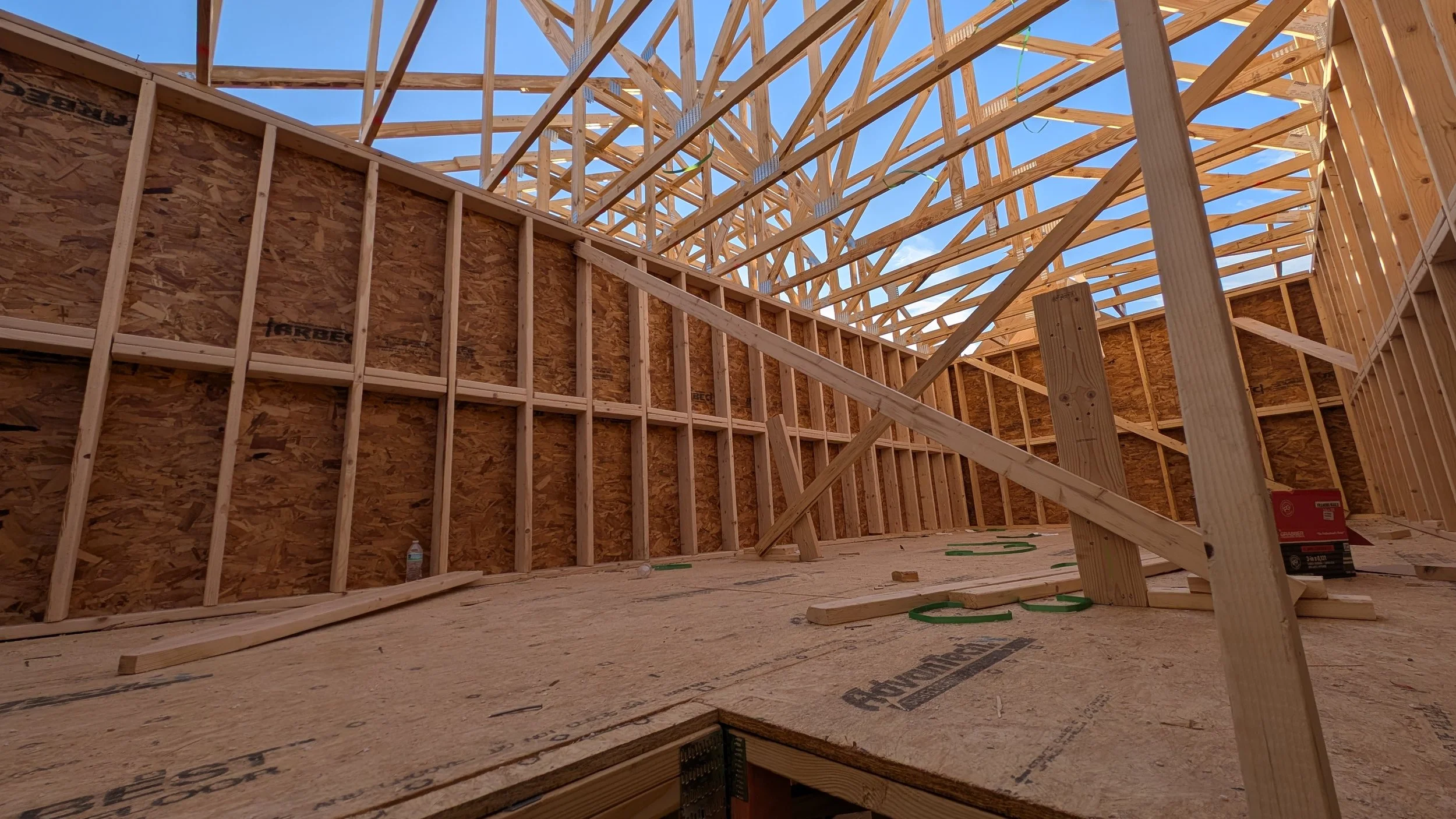 Interior view of a house under construction with wooden framing and roof trusses installed.
