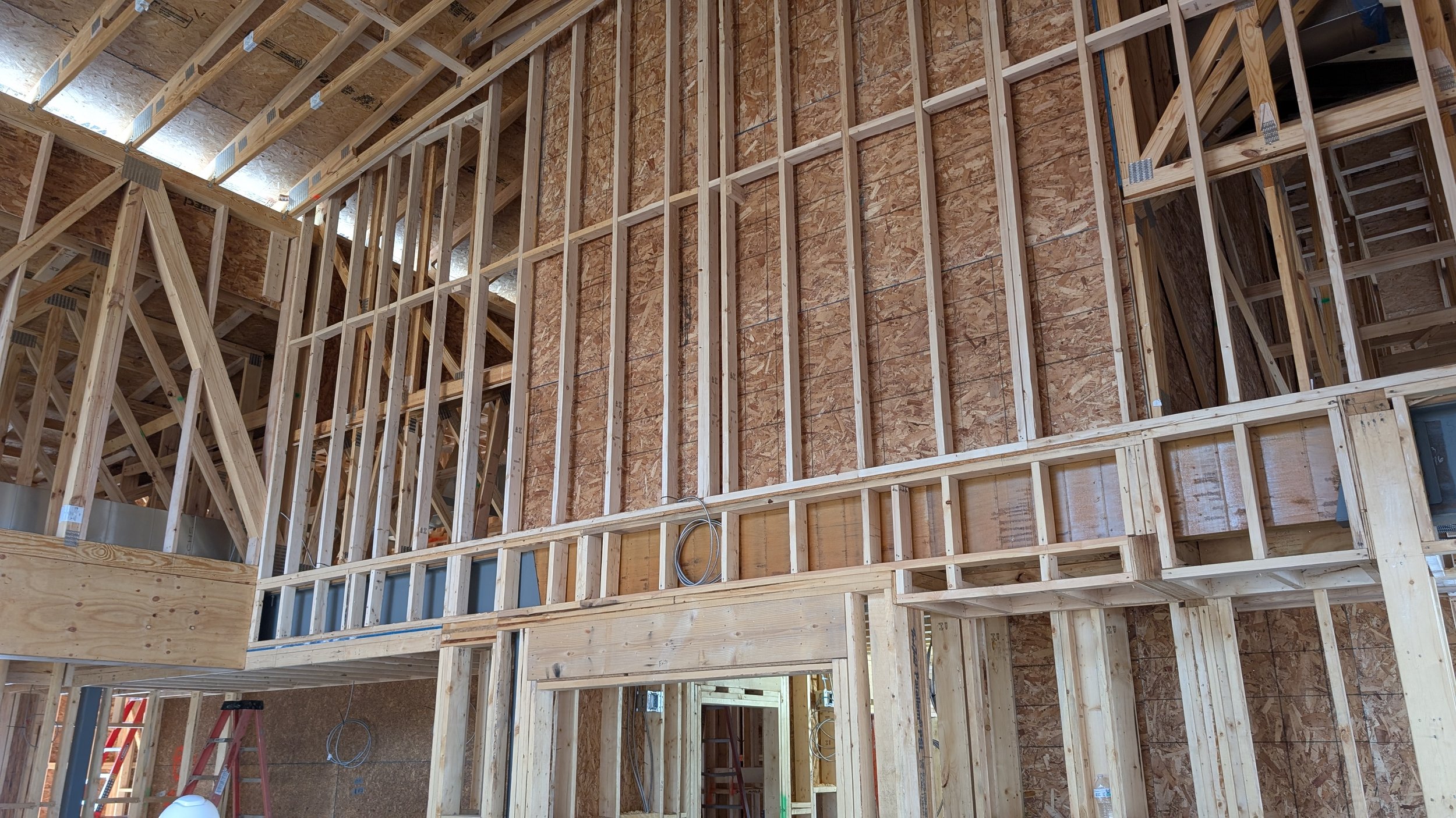 Interior view of a building under construction with exposed wooden framing, studs, and partial wall sheathing.