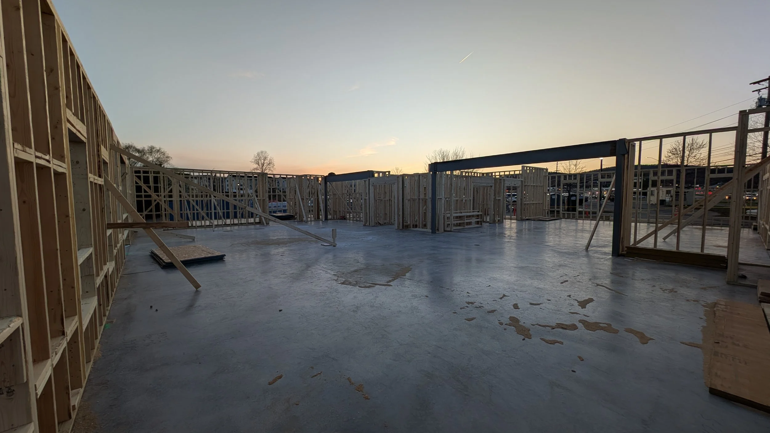 Construction site with wooden framing for a building, concrete floor, and an open view at sunset.