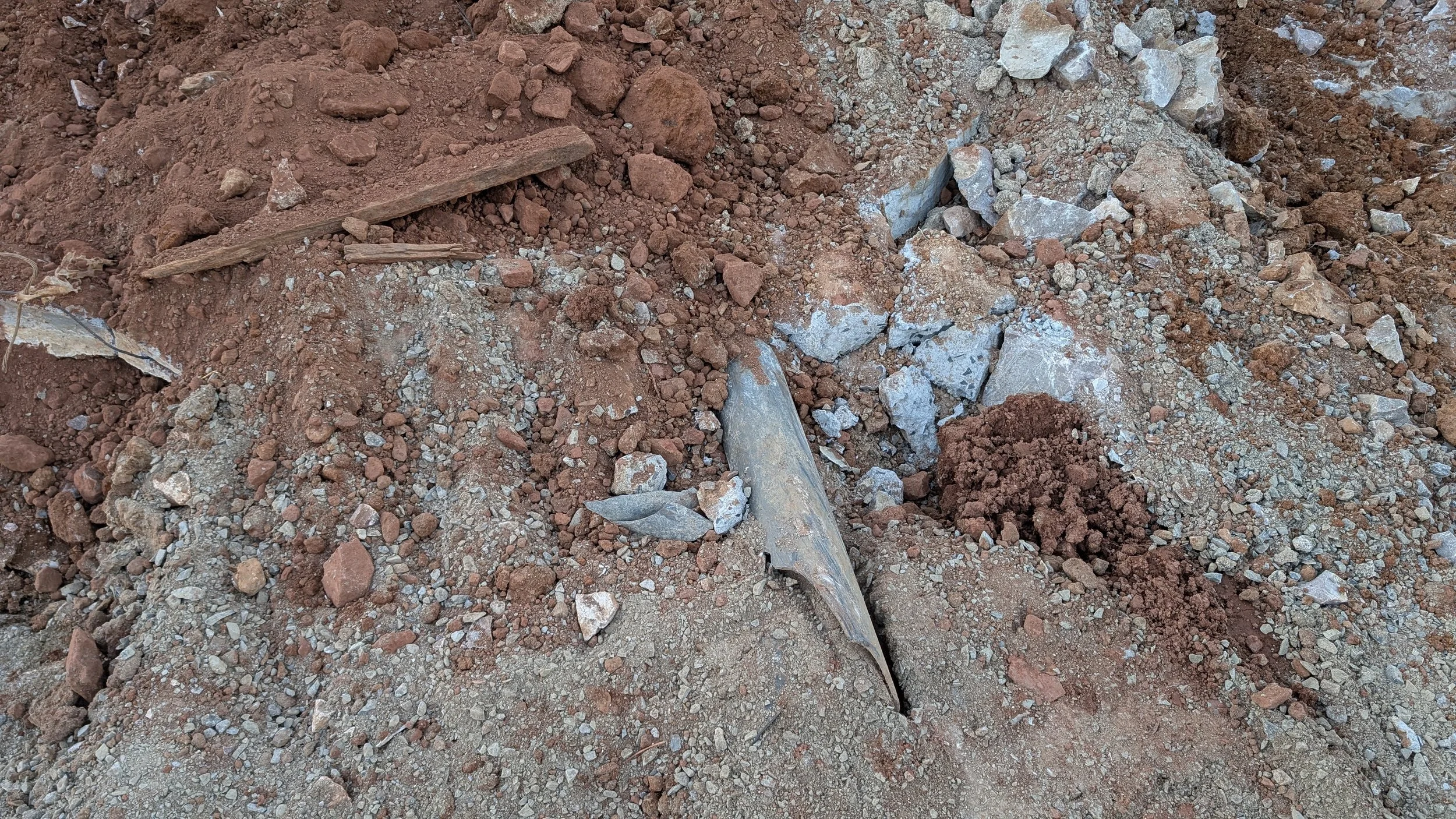 Scattered rocks, dirt, and debris on a construction site or excavation area, with a small metallic object partially buried in the soil.