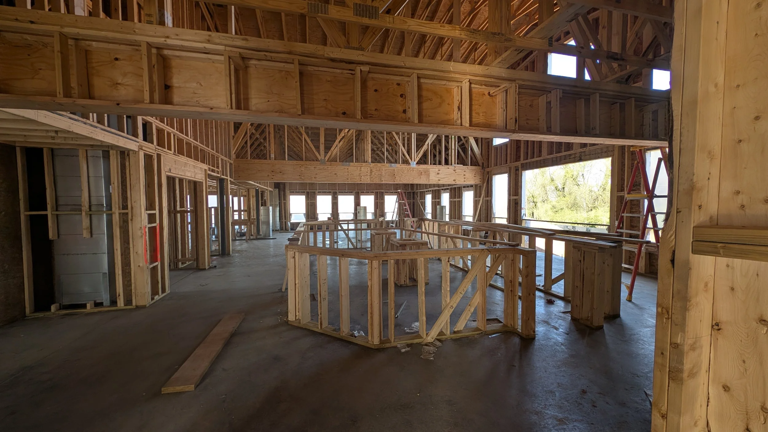 Interior view of a building under construction with wooden framing, scaffolding, and large windows.