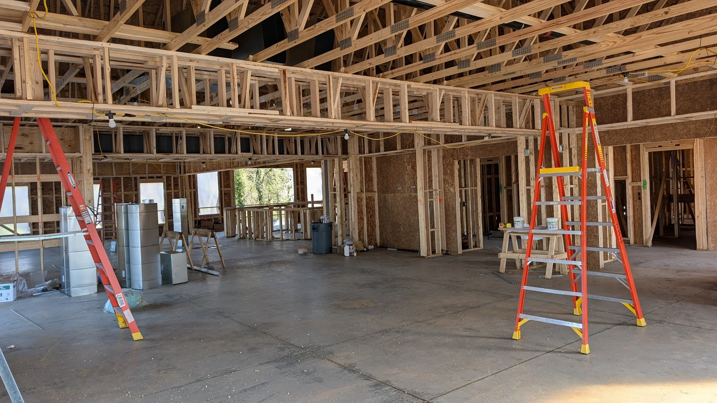 Construction site of a house with exposed wooden framing, ladders, and tools inside, preparing for drywall or finishing work.