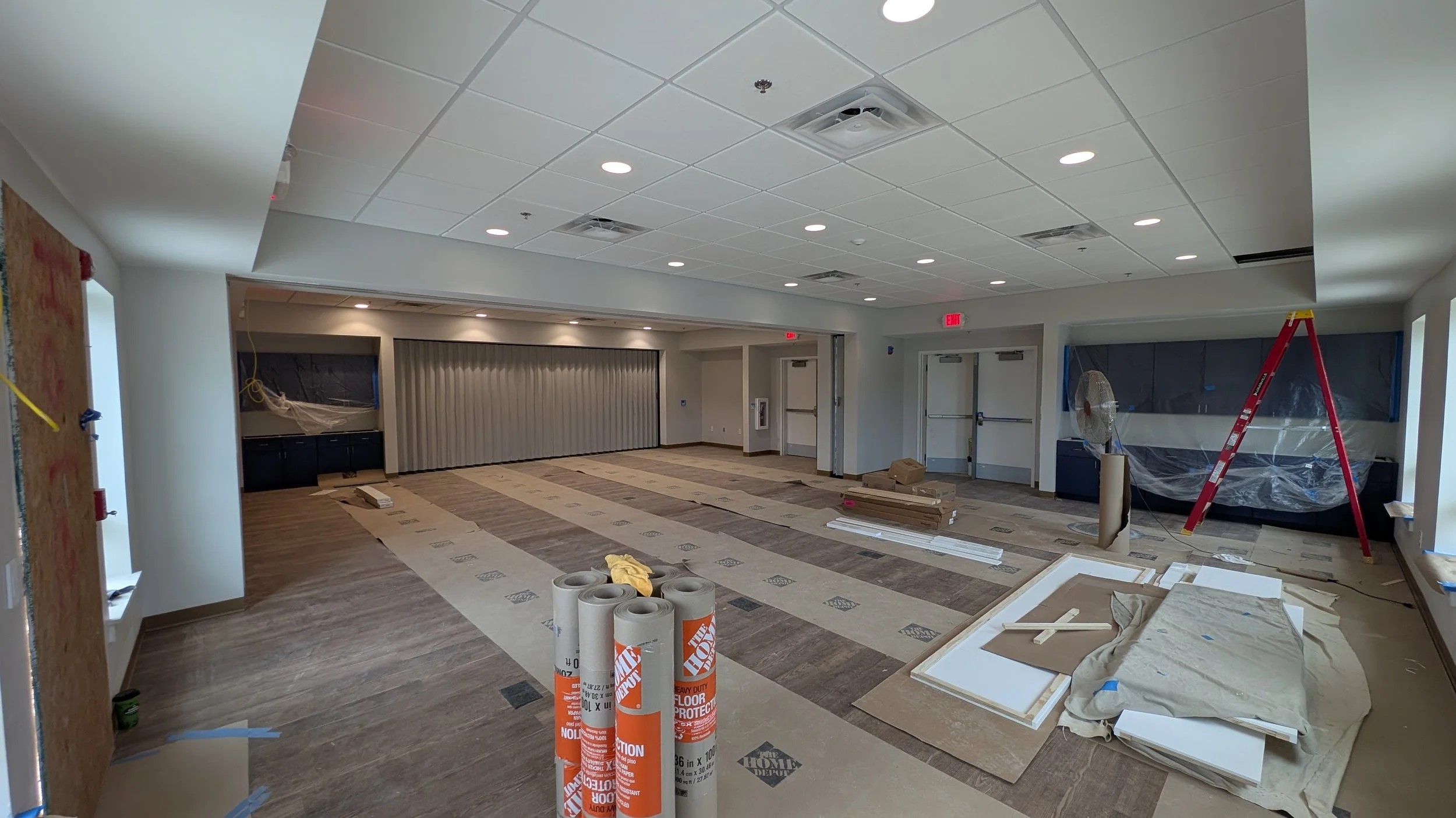 Interior of a room under renovation with construction materials, ladder, and covered windows.