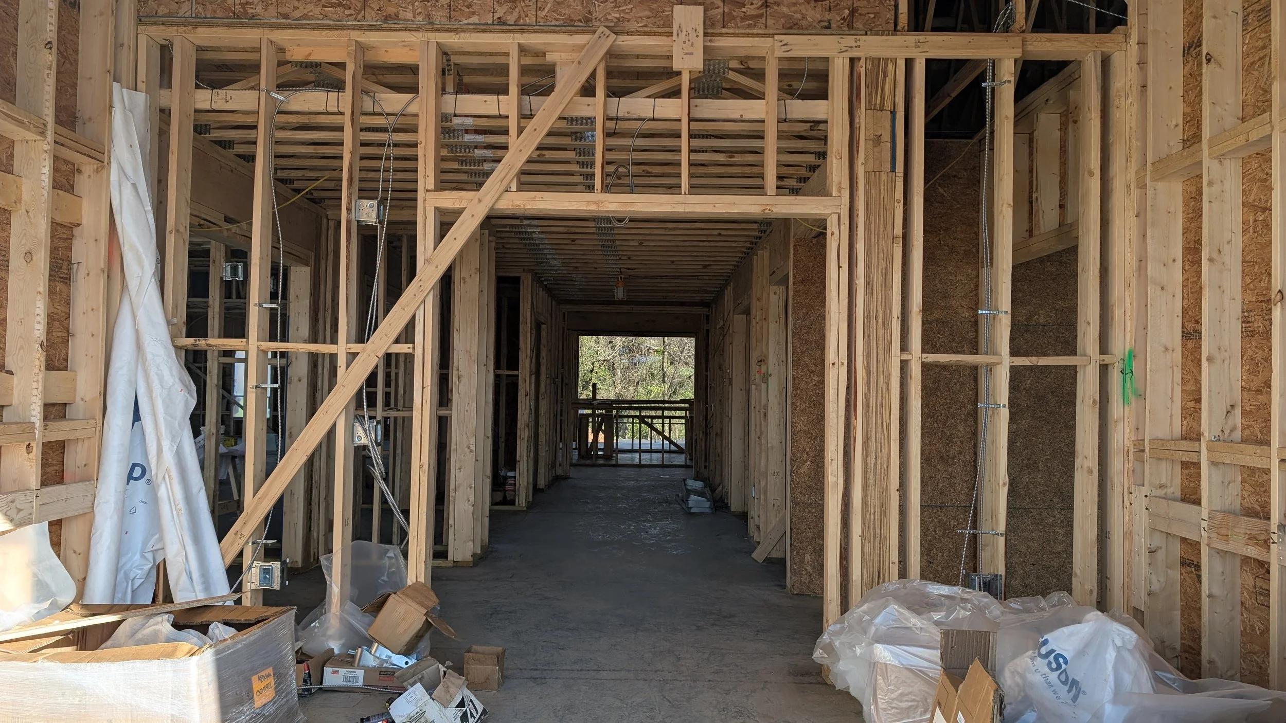 Interior of a building under construction with wooden framing, exposed wiring, and construction materials and debris on the floor.