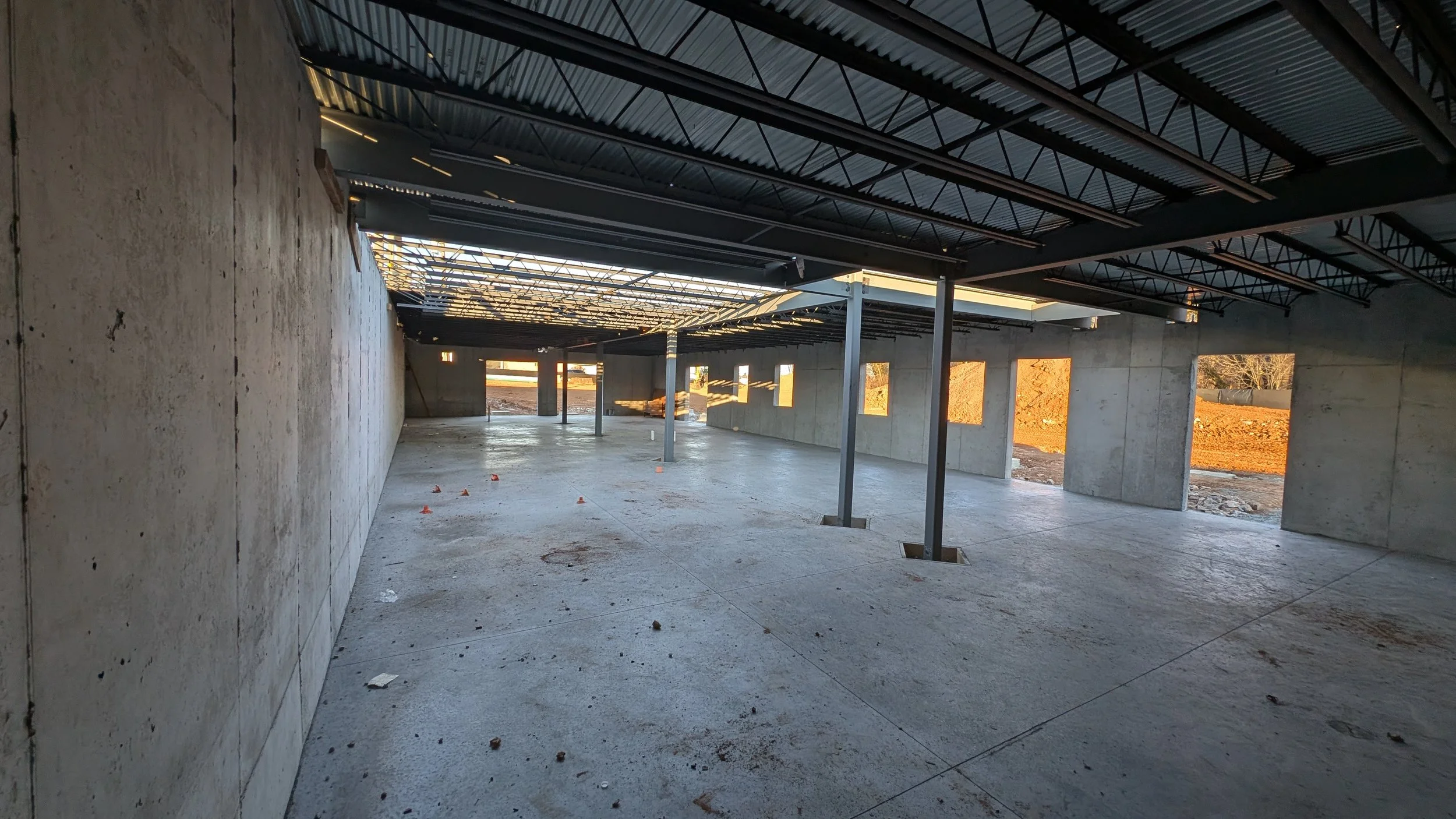 Construction site with unfinished building showing concrete walls, exposed steel roof framing, support columns, and open window spaces.