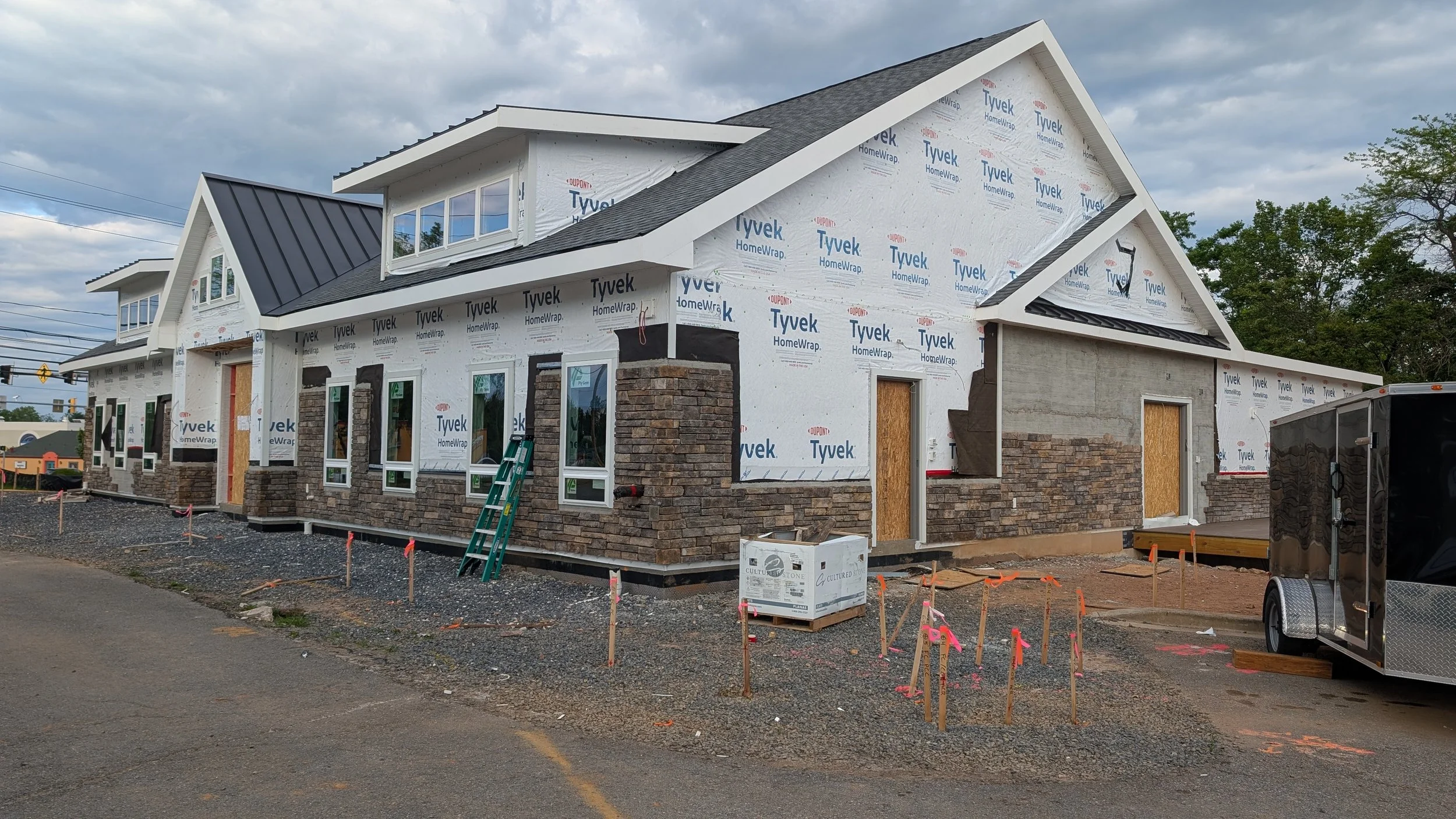 Under construction residential building with stone veneer, windows, and partially installed siding, construction materials, and equipment around the site.