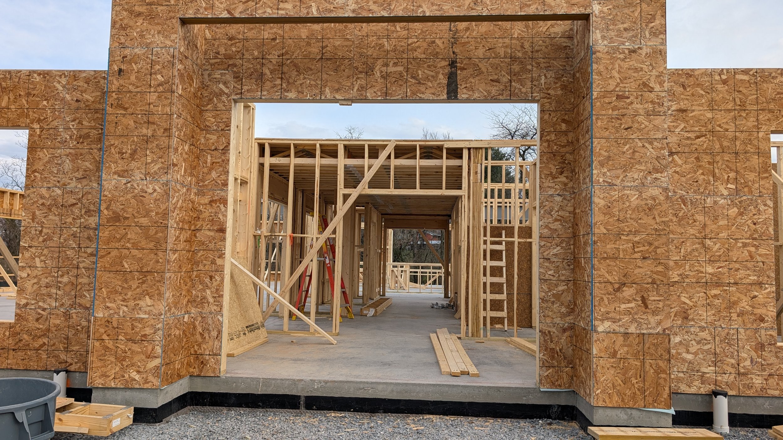 Construction site with wooden framing for a building, outside walls covered with oriented strand board (OSB) sheathing, and construction tools and materials present.