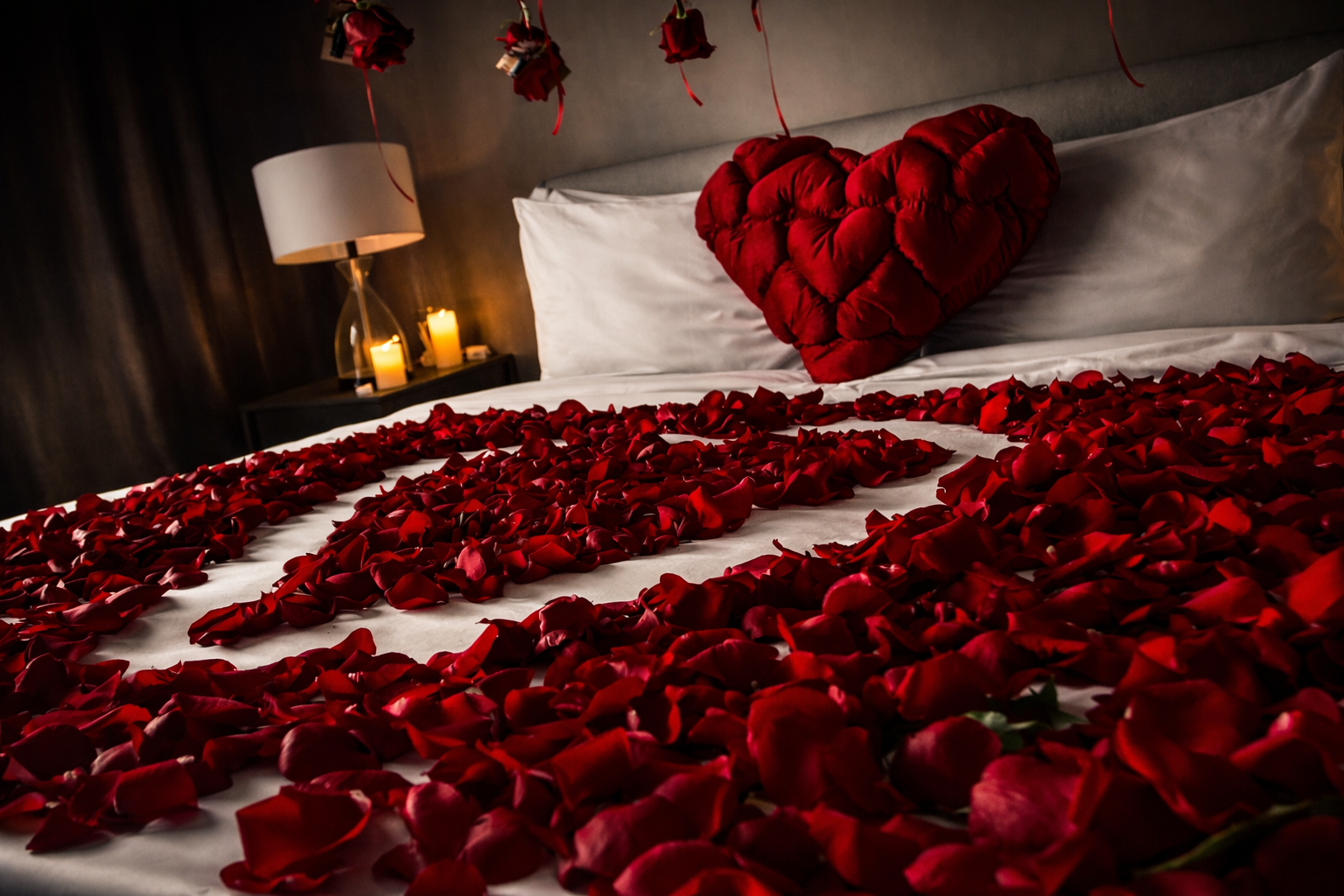 Bouquet of red roses on a bed with rose petals, a box of white strawberries dipped in chocolate with pink roses, in a hotel room.