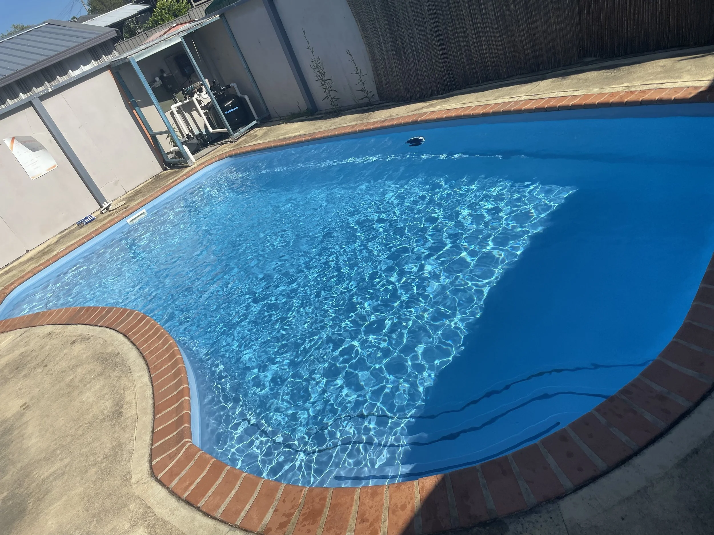 a blue pool with surrounding brown brick pavers