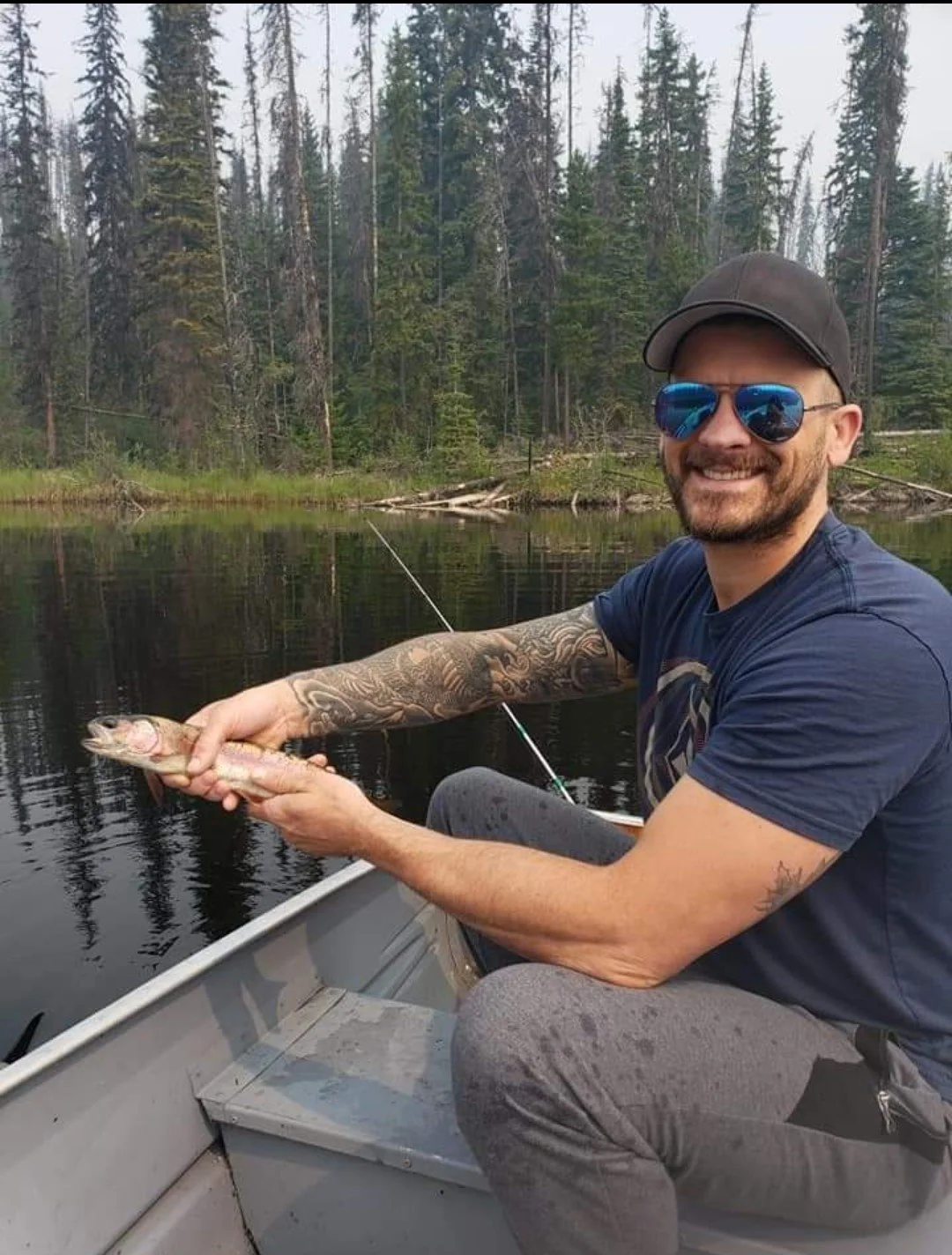 Man holding a fish in a boat on a forested lake