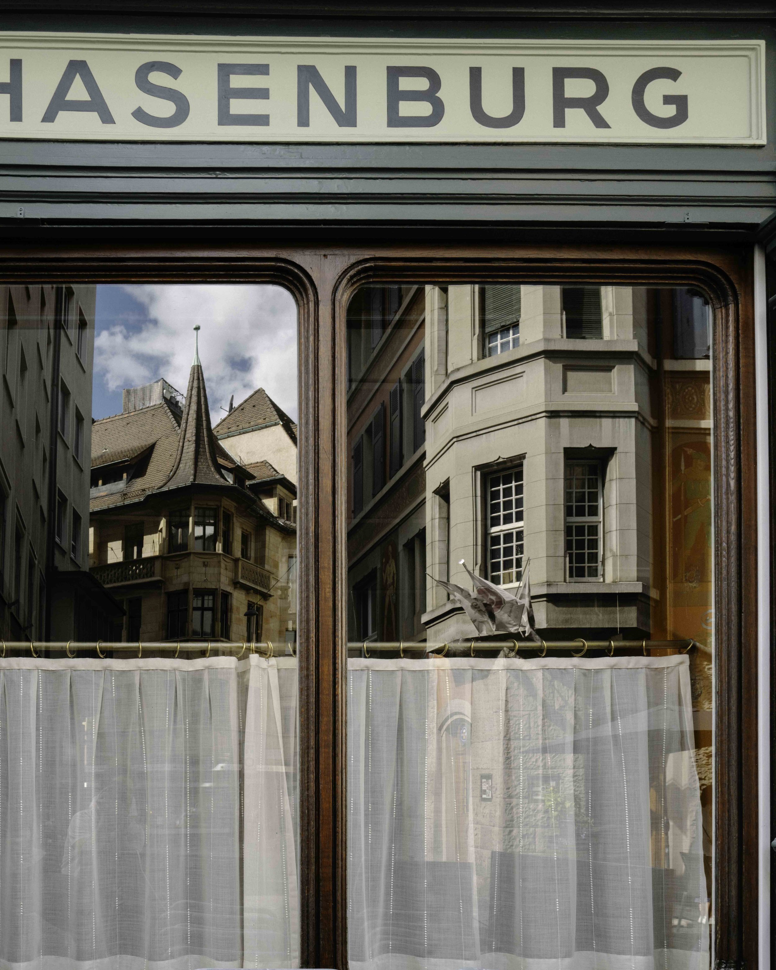 Enseigne et vitrine du restaurant Hasenburg, reflet de l'architecture de la vieille ville de Bâle.
Sign and window of the Hasenburg restaurant, reflecting Basel's old town architecture.
Schriftzug und Schaufenster des Restaurants Hasenburg, mit Spieg