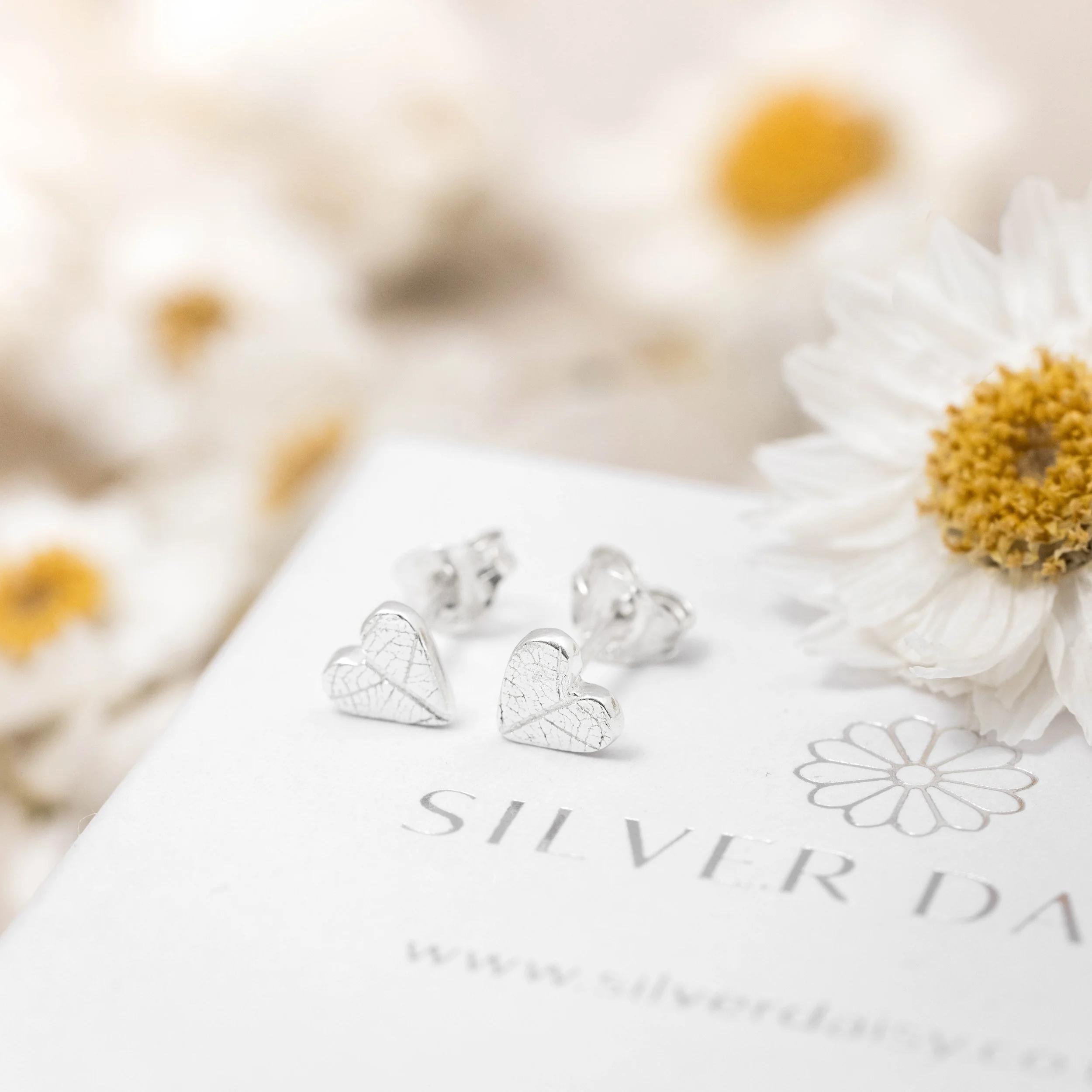 Mini sterling silver heart stud earrings with delicate leaf vein texture, polished finish, and butterfly backs.