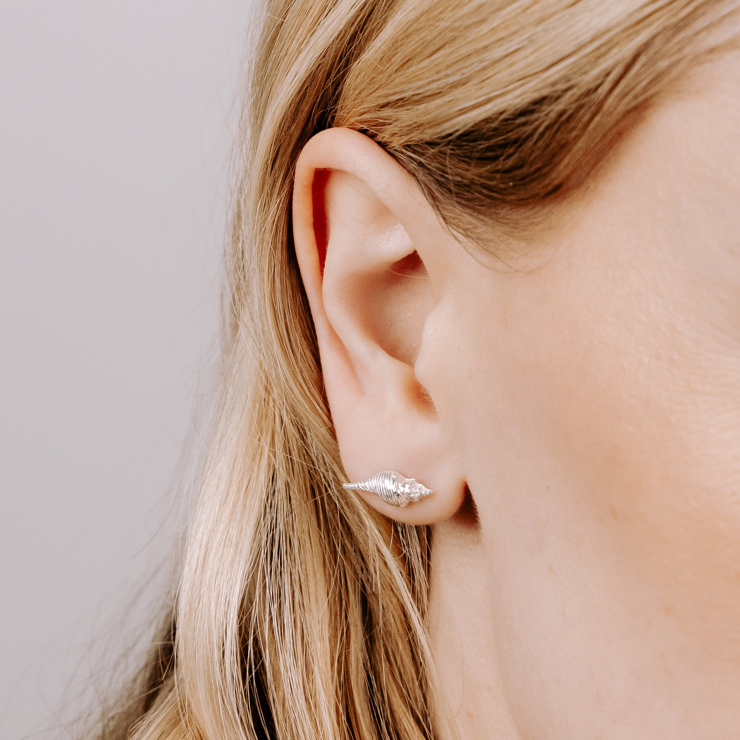 Dainty sterling silver conch shell stud earrings with polished finish, inspired by coastal seashell designs.