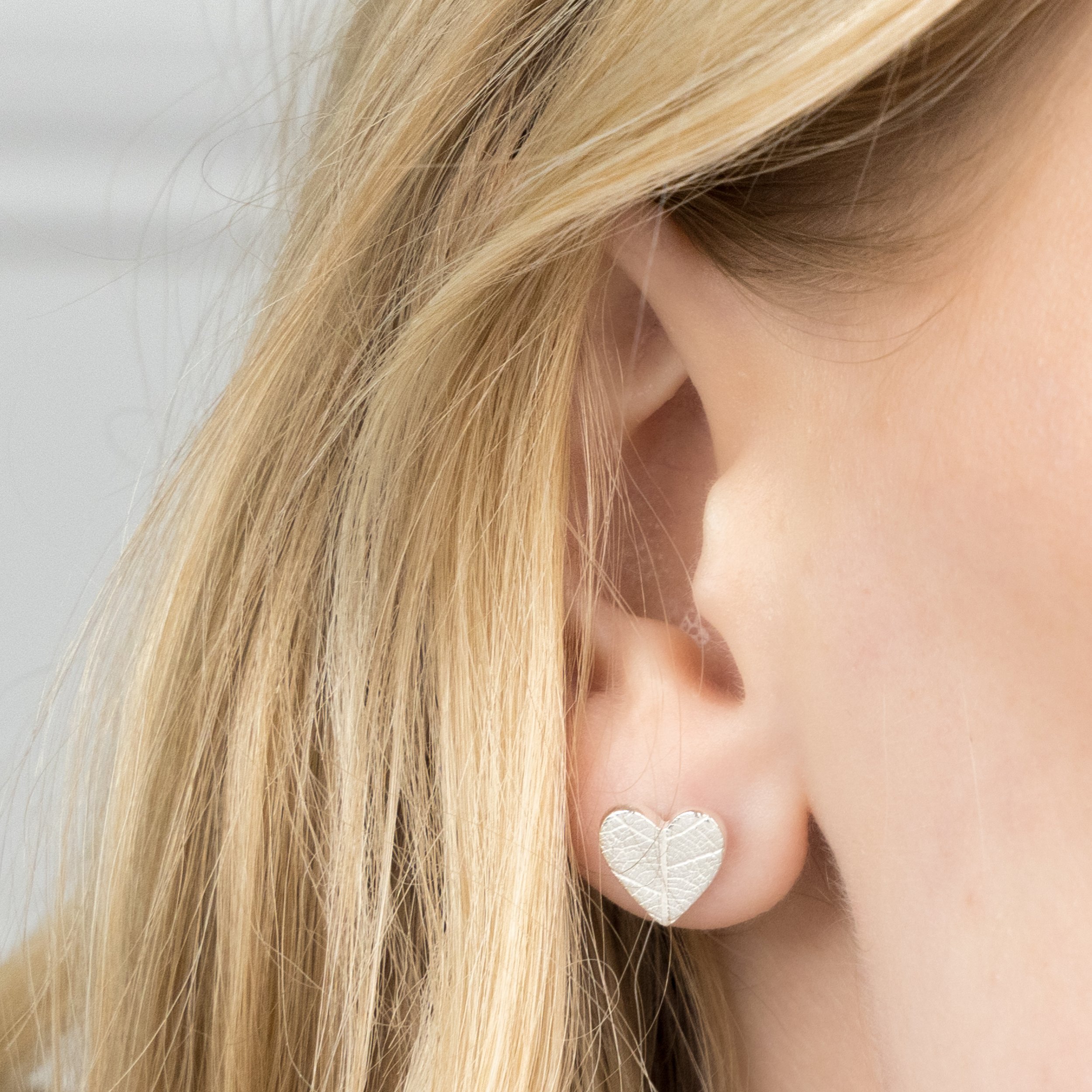 Sterling silver heart stud earrings with delicate imprinted leaf texture on a polished finish.