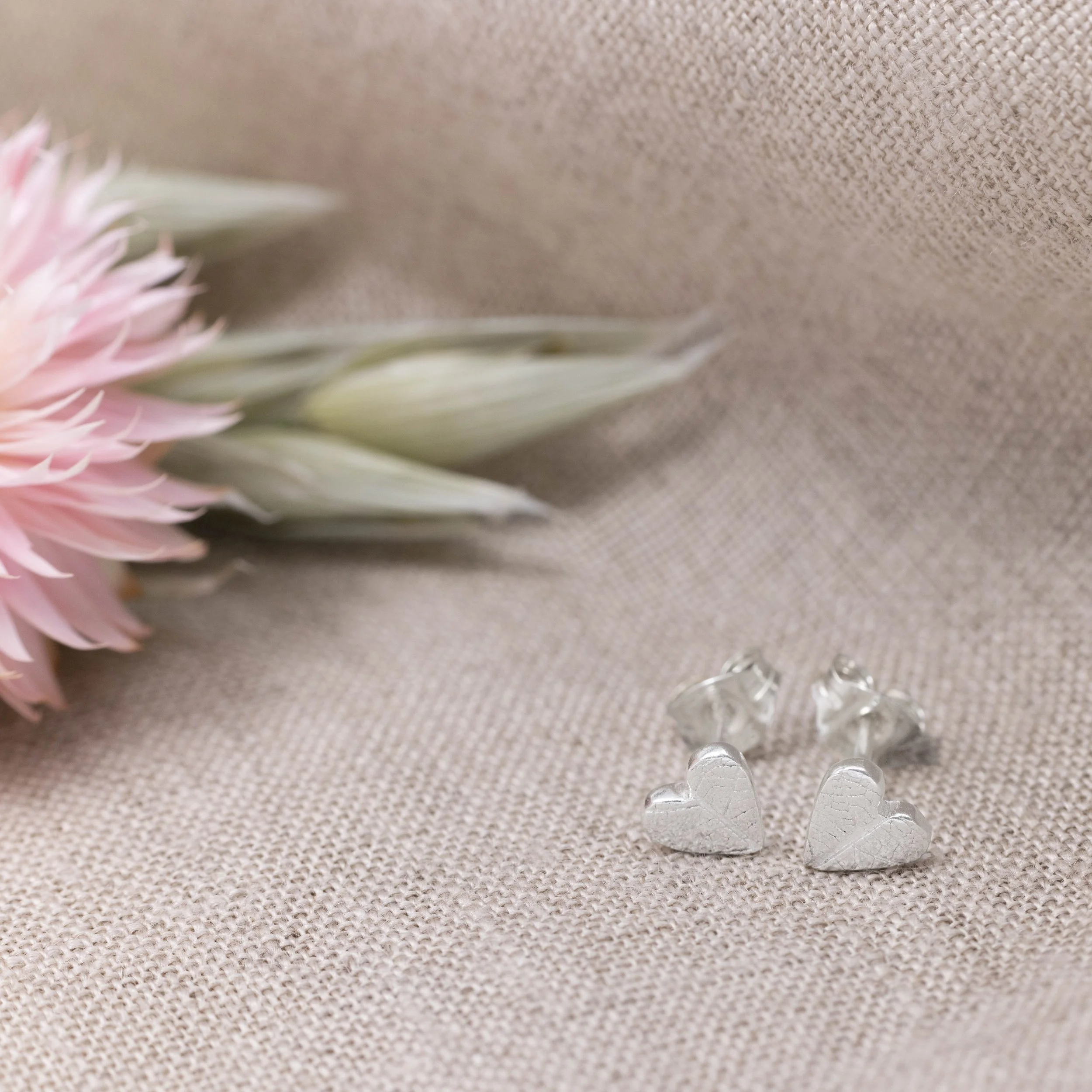Mini sterling silver heart stud earrings with delicate leaf vein texture, polished finish, and butterfly backs.