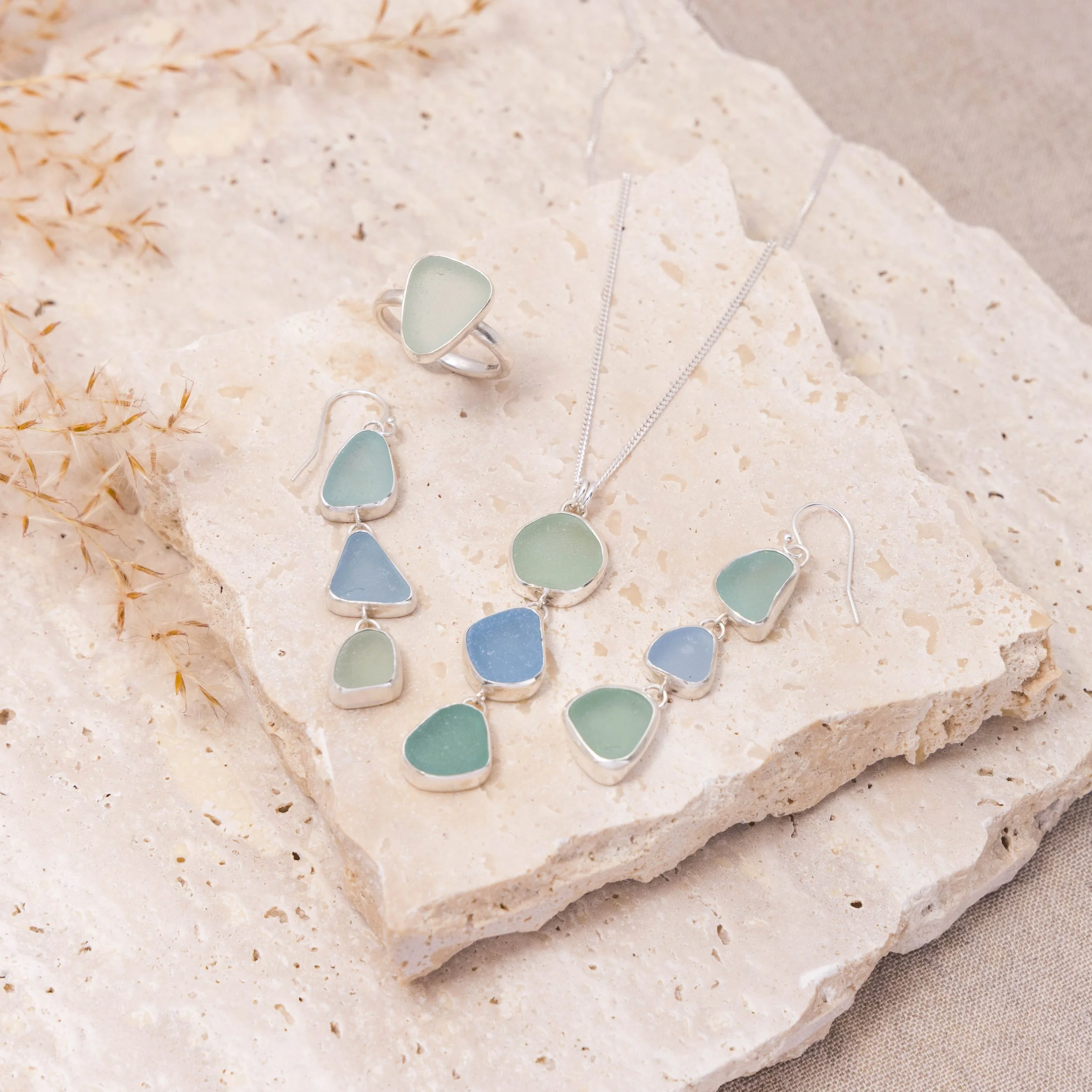 Sterling silver pendant necklace with cascading multi-coloured sea glass drops in green and blue tones, inspired by coastal style.