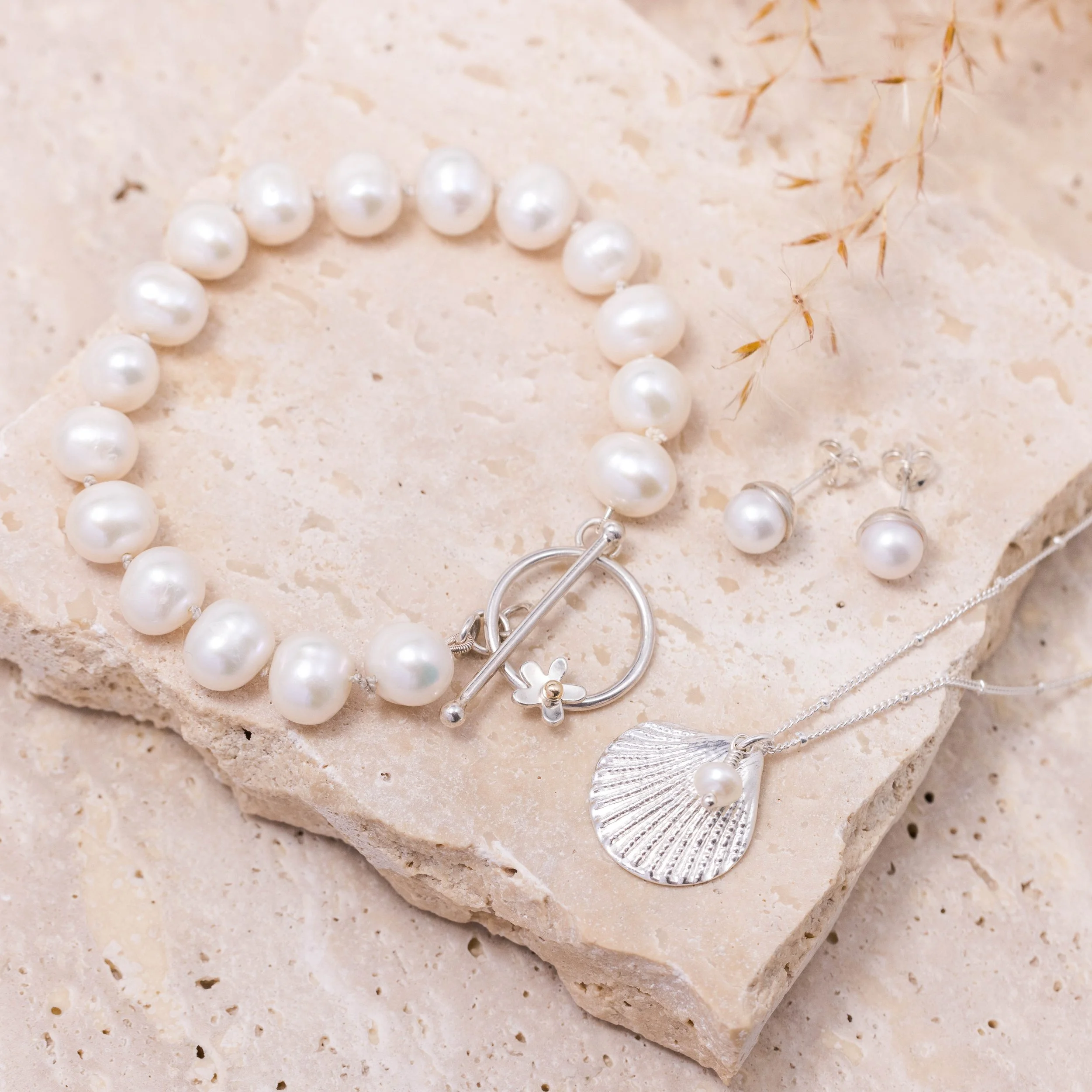 Silver scallop shell pendant necklace with a single white pearl on a delicate chain, inspired by coastal jewellery design.