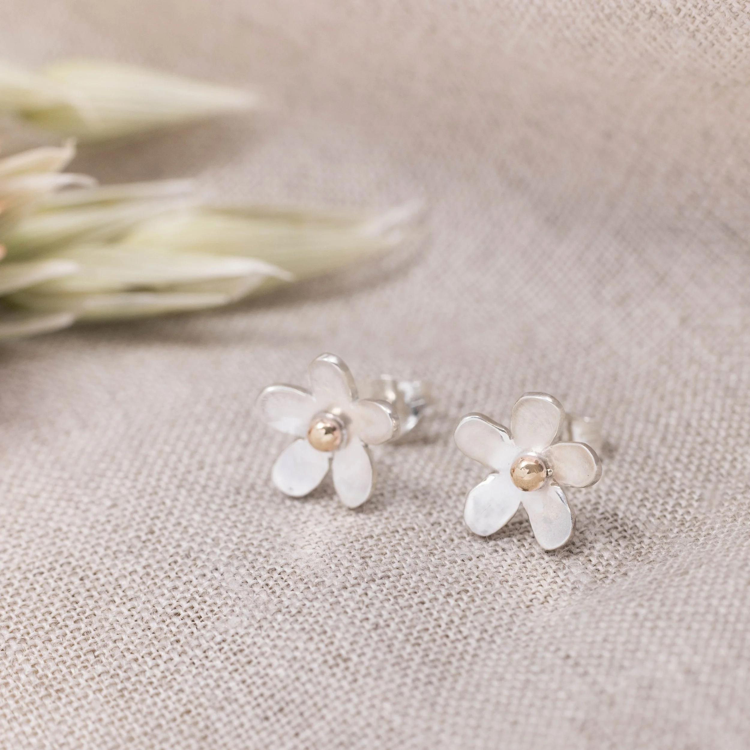 Handmade silver daisy stud earrings with polished petals and 9ct gold stamen centres.
