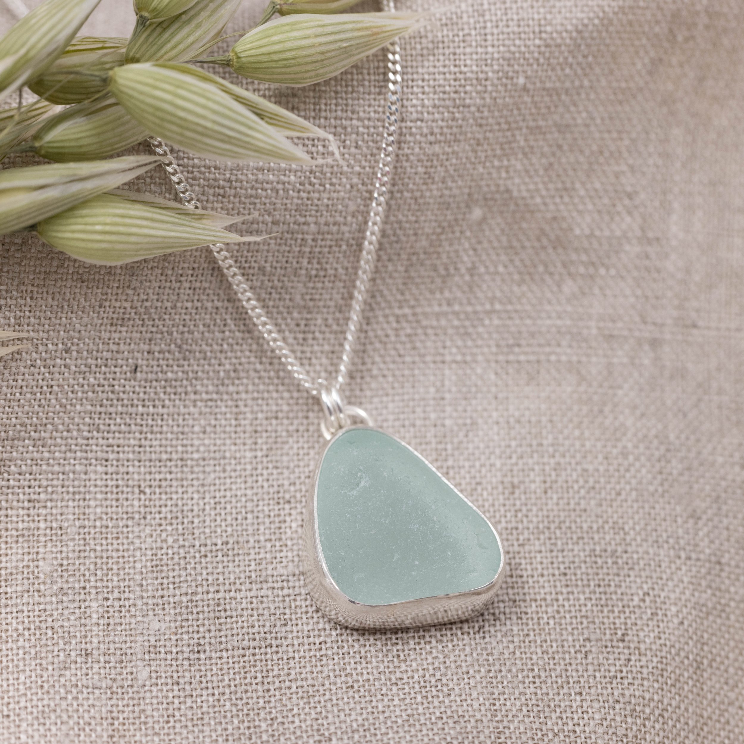Aqua sea glass pebble set in polished silver on a delicate chain, coastal-inspired handmade necklace.