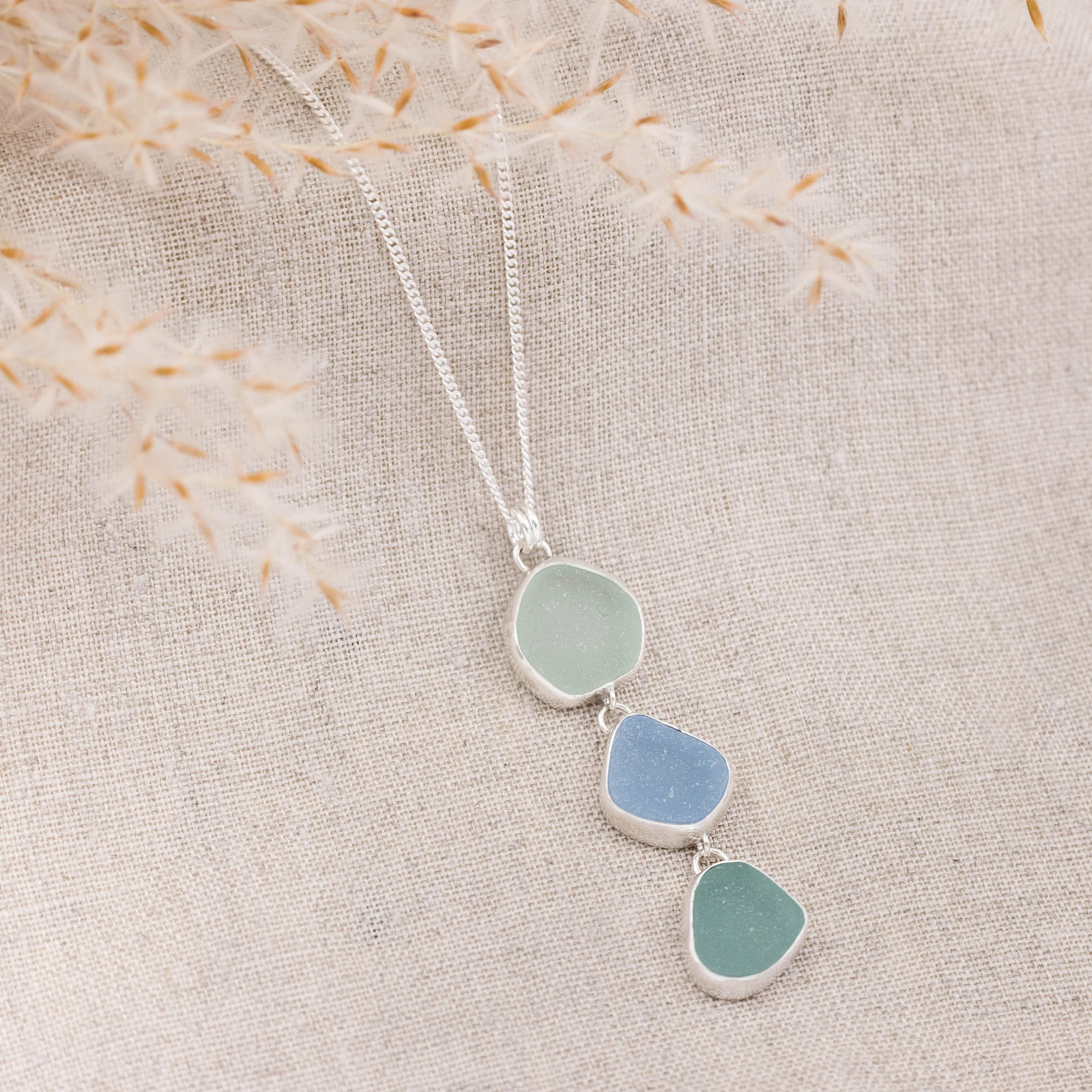 Sterling silver pendant necklace with cascading multi-coloured sea glass drops in green and blue tones, inspired by coastal style.