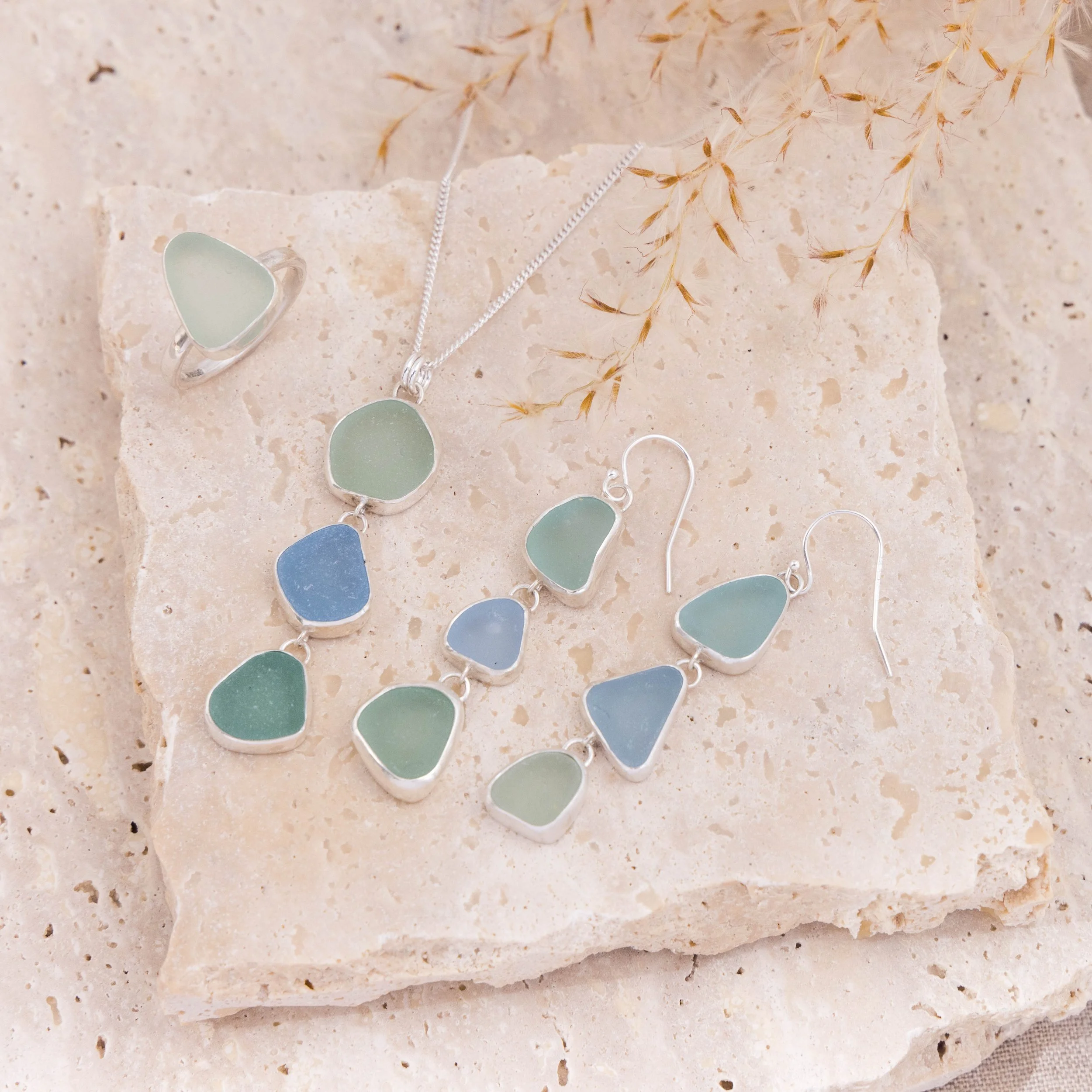 Sterling silver drop earrings with cascading multi-coloured sea glass pieces in green and blue tones on delicate ear wires. Coastal inspired jewellery design.