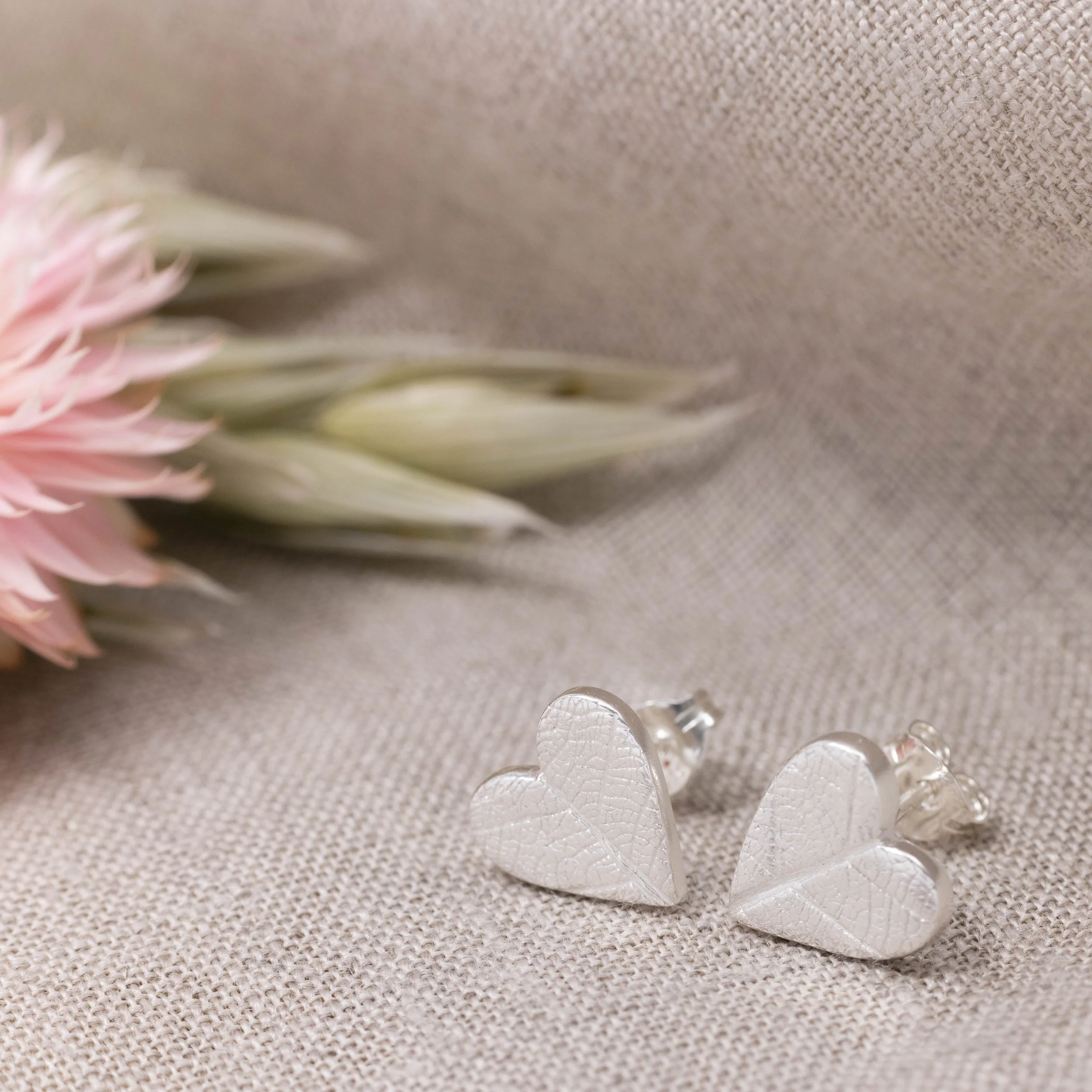 Sterling silver heart stud earrings with delicate imprinted leaf texture on a polished finish.