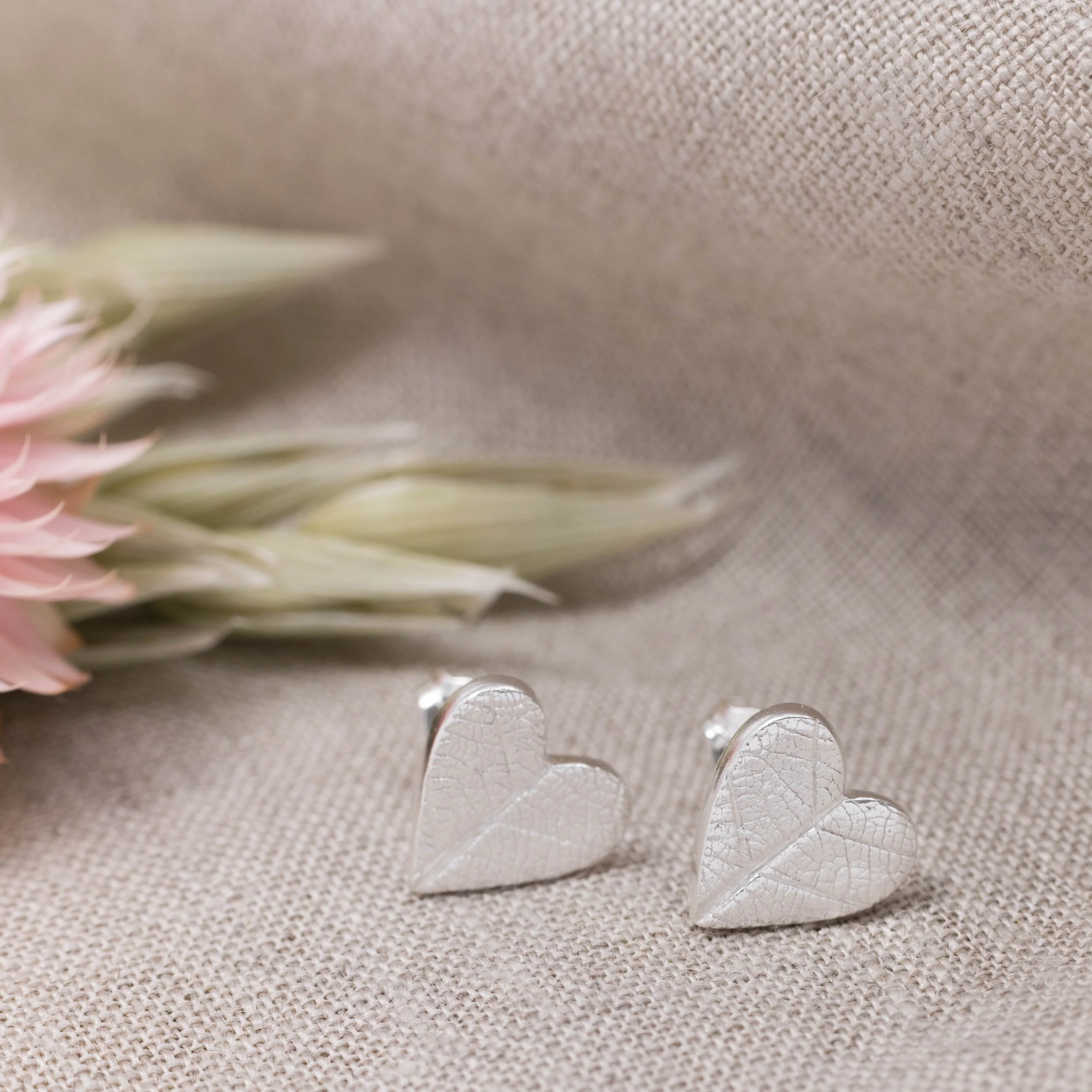 Sterling silver heart stud earrings with delicate imprinted leaf texture on a polished finish.
