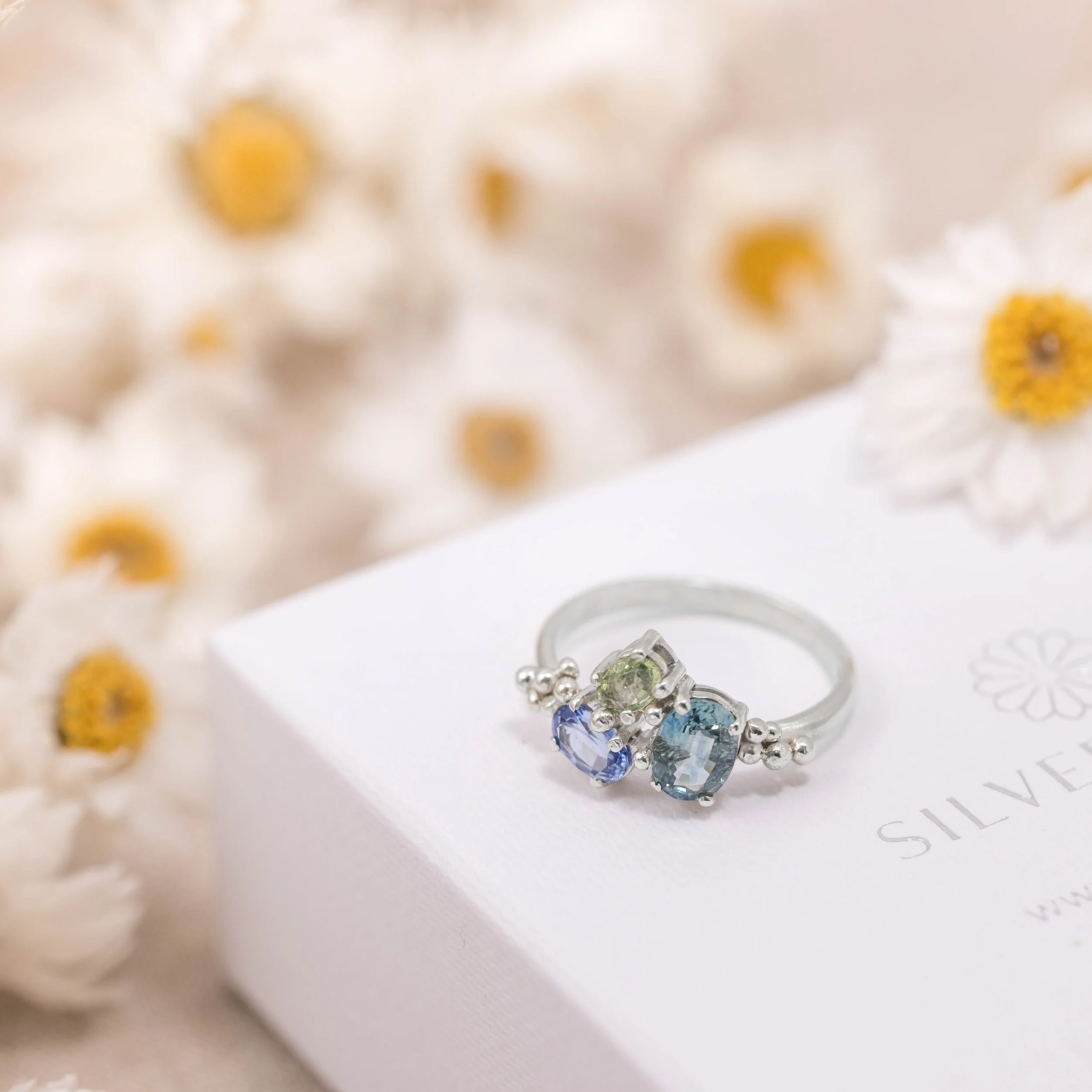 White gold ring with a cluster of oval blue and green sapphires in a seascape-inspired design.