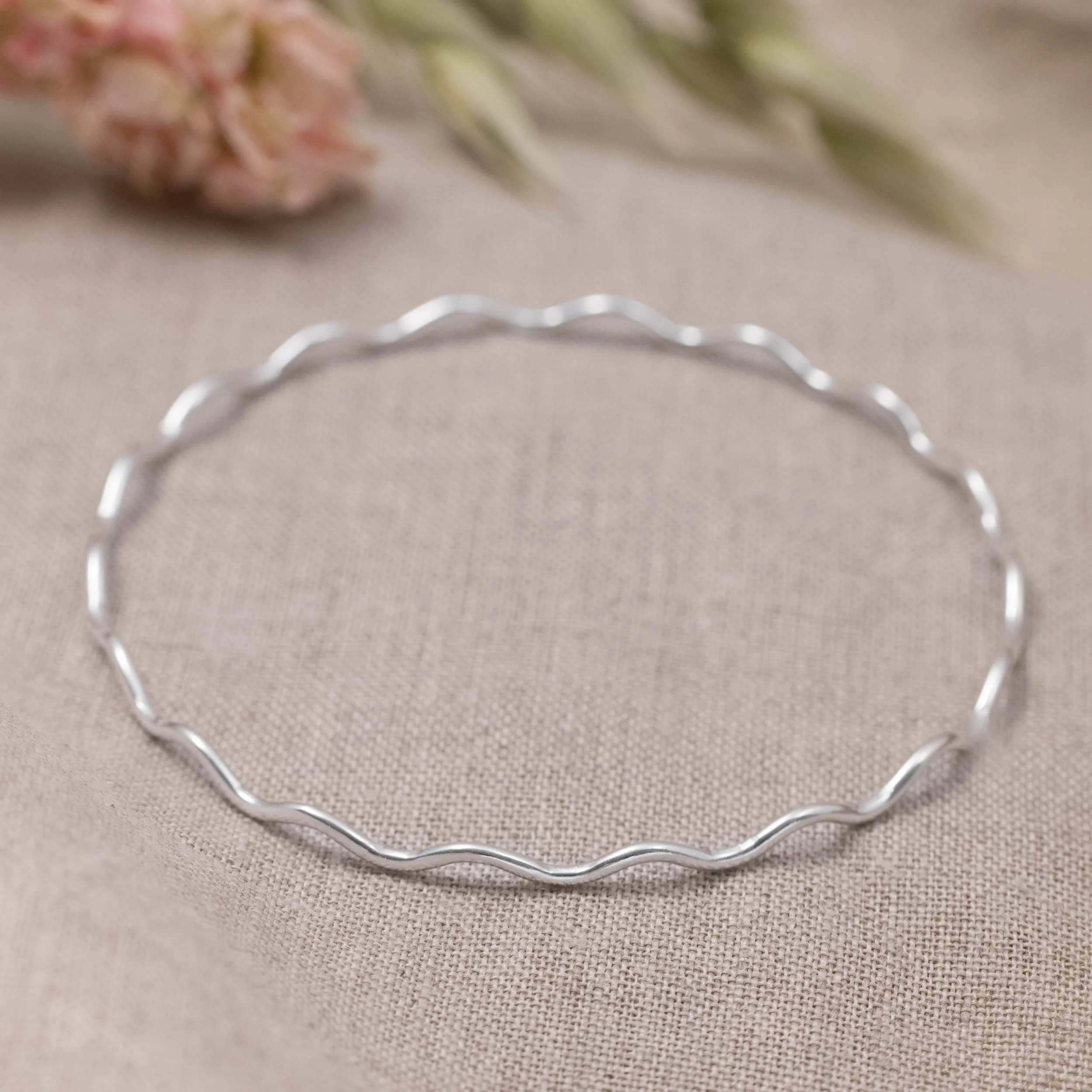 Sterling silver scallop stacking bangle with softly curved edges and polished wave detailing, designed for layering or elegantly worn alone.