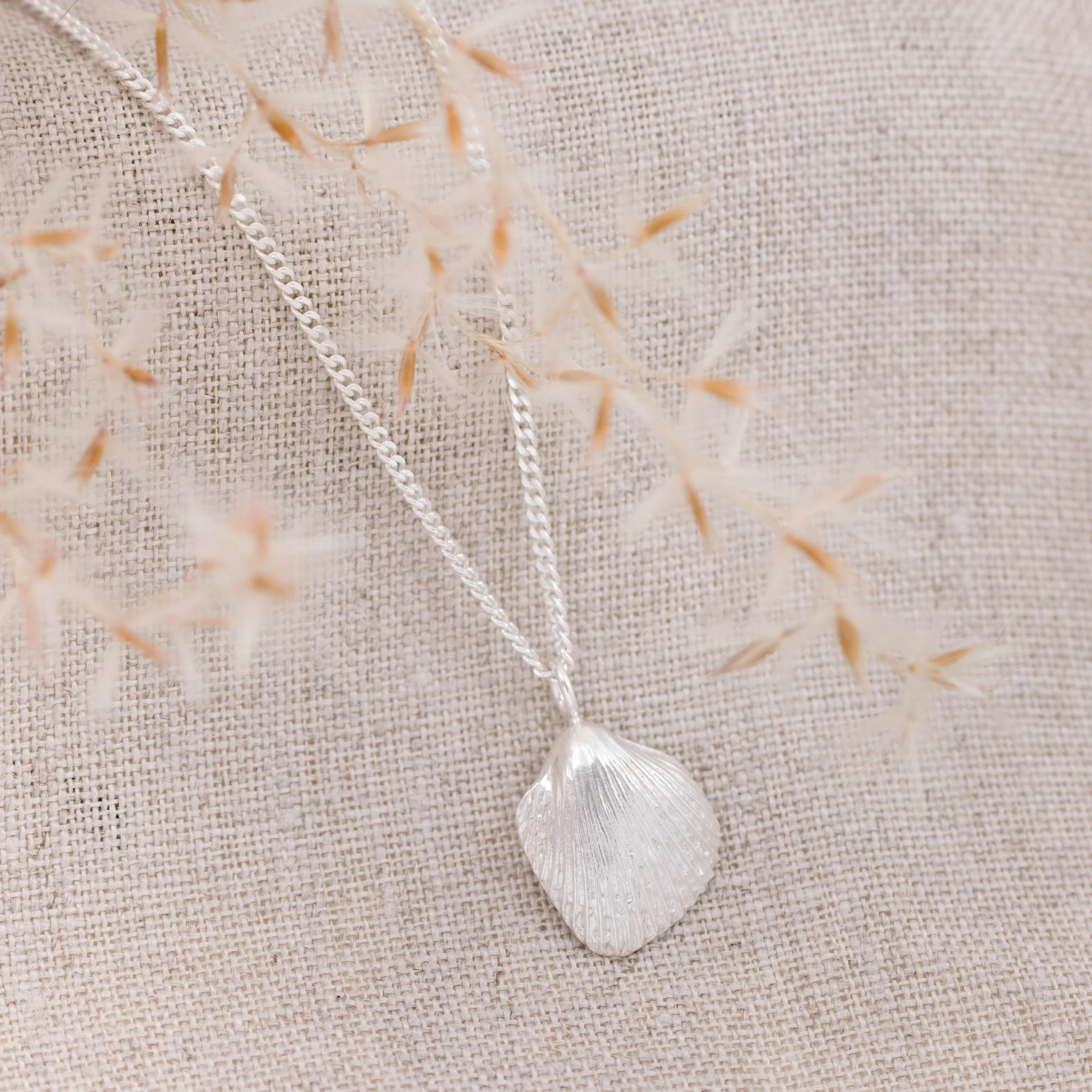Sterling silver cockle shell pendant necklace with fine detailing on a delicate silver chain, inspired by coastal beachcombing.