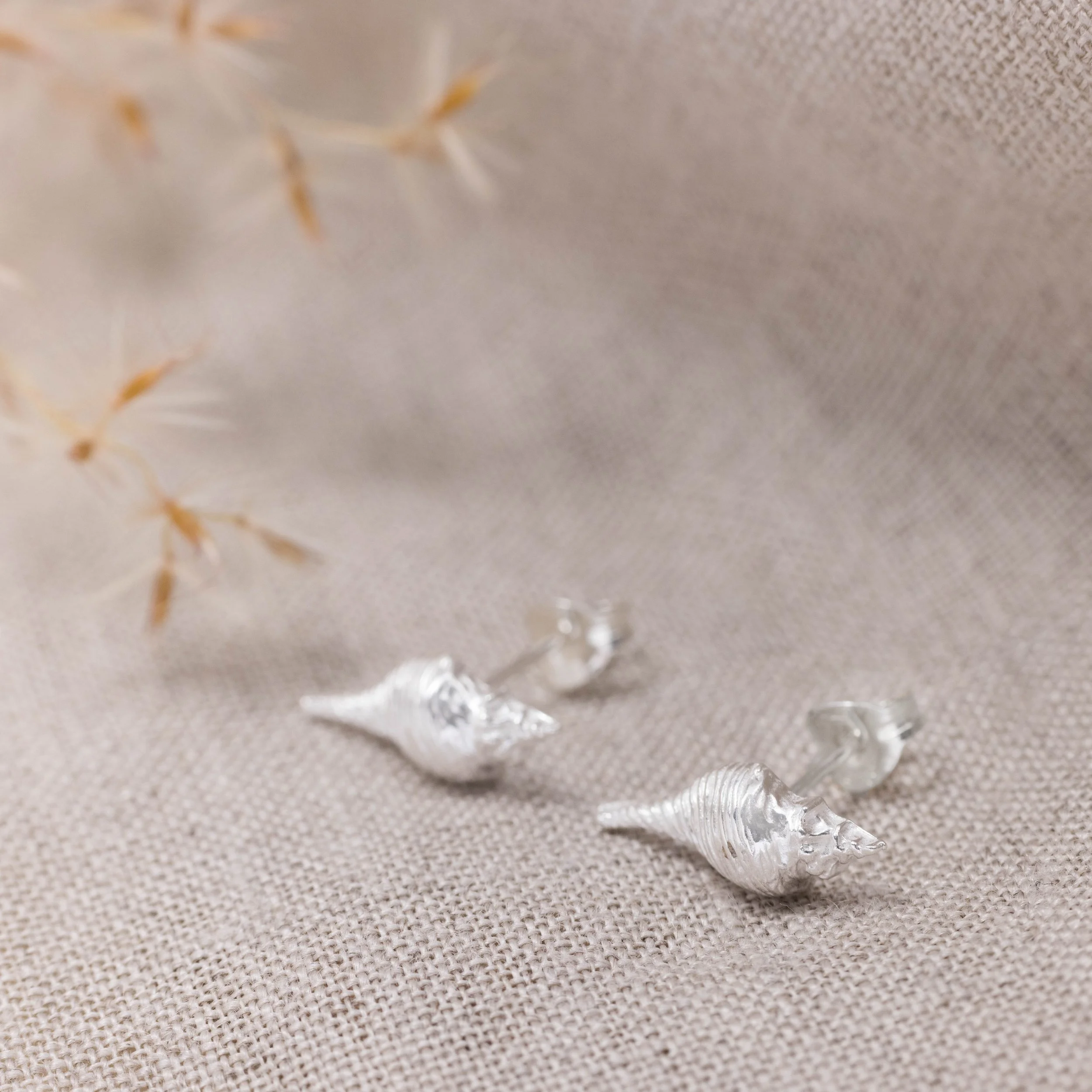Dainty sterling silver conch shell stud earrings with polished finish, inspired by coastal seashell designs.