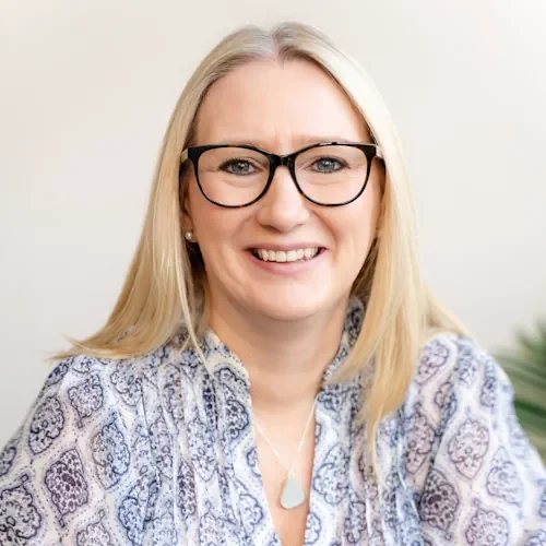 A smiling woman with blonde hair, wearing glasses and a patterned blouse.