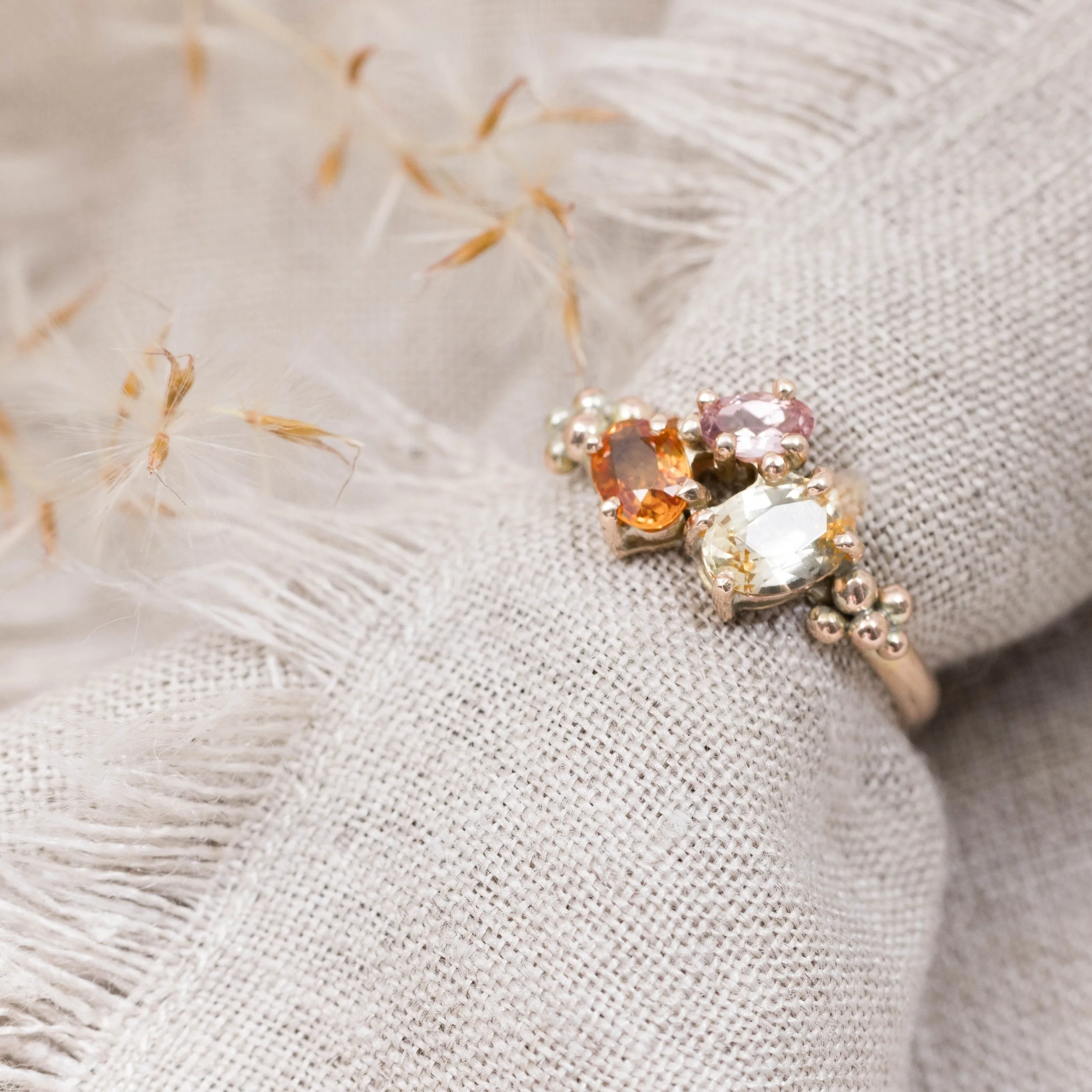 Rose gold ring with an oval orange sapphire centre surrounded by a cluster of round pink and yellow sapphires.