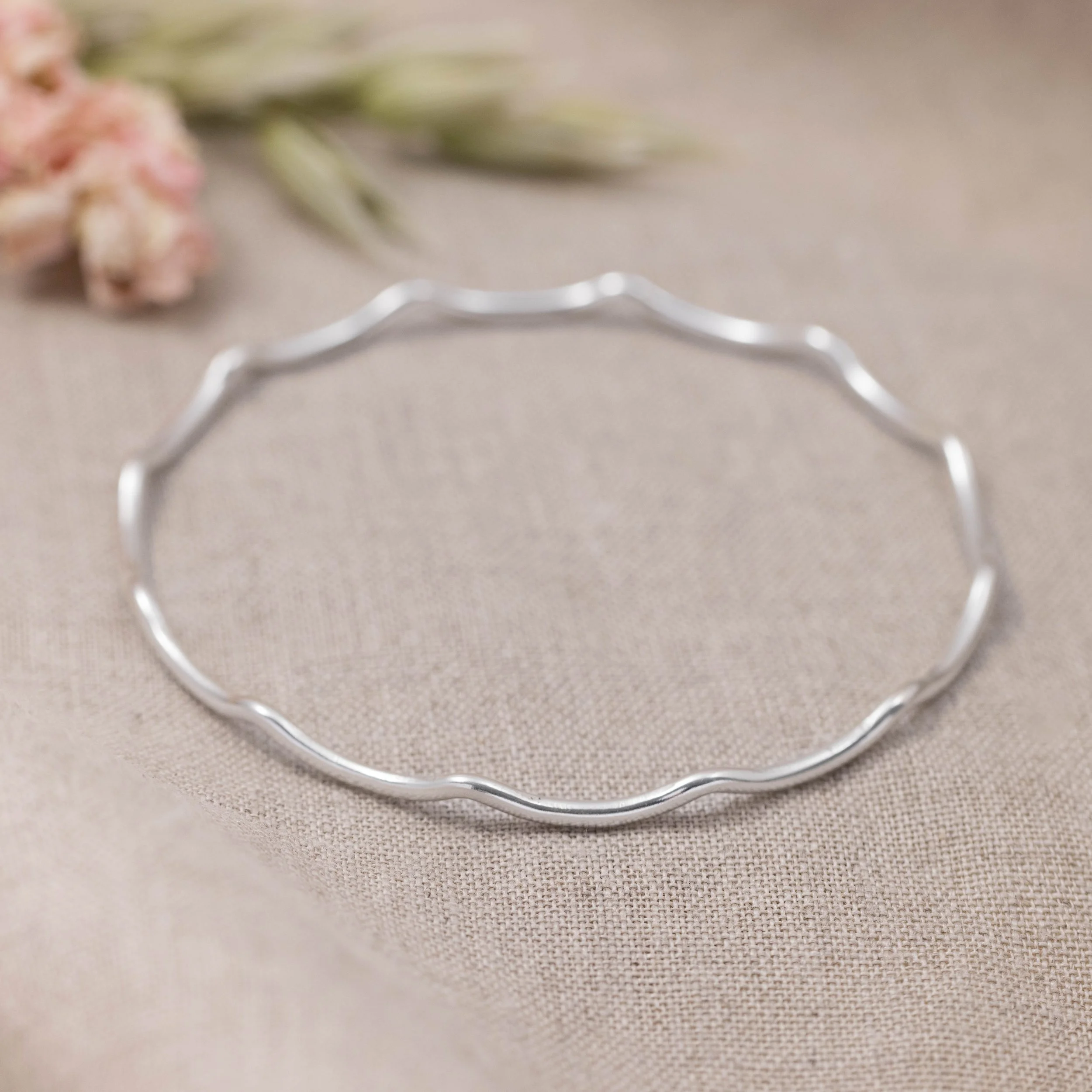Slim sterling silver stacking bangle with a polished wave design, perfect for layering in a modern minimalist style or simply worn alone.