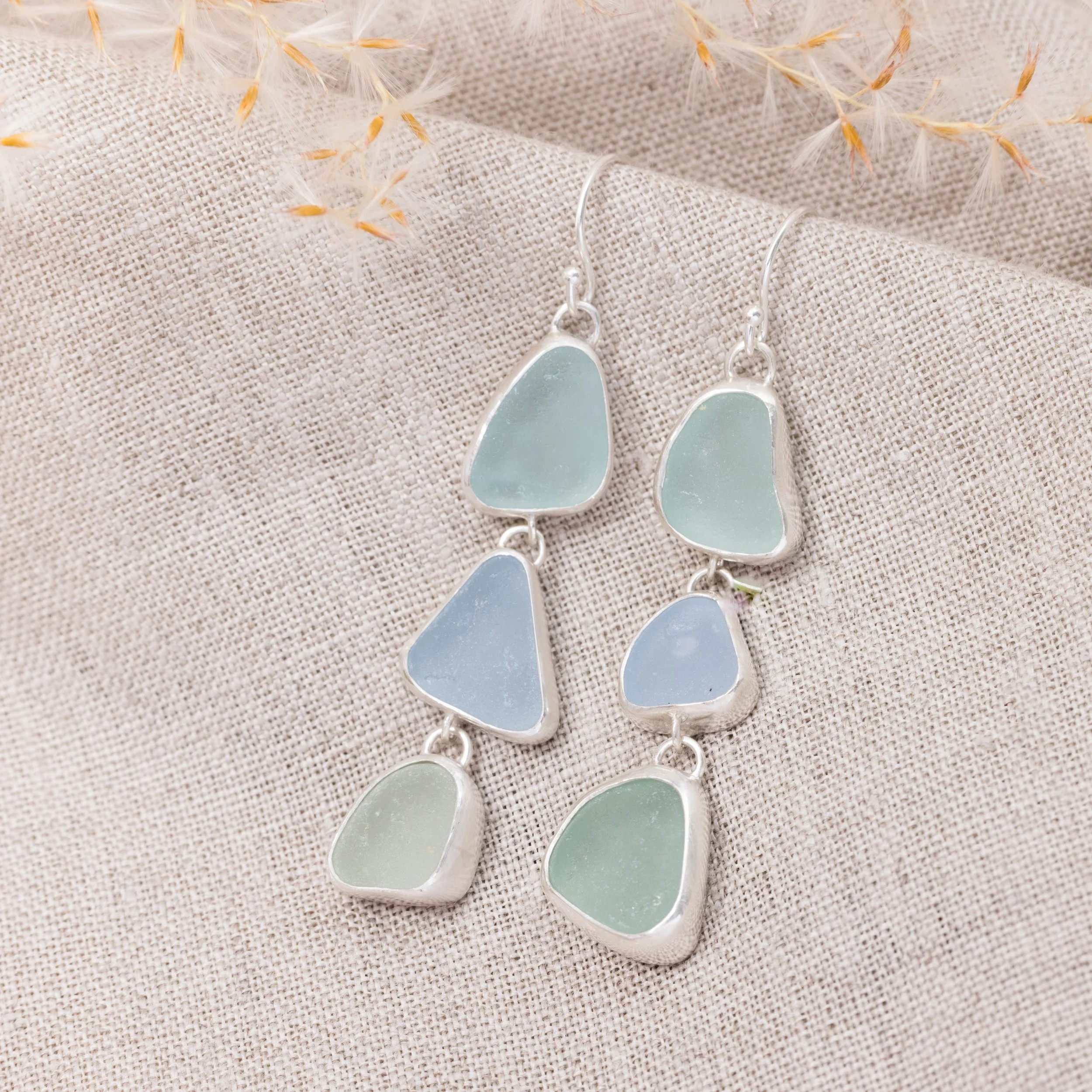 Sterling silver drop earrings with cascading multi-coloured sea glass pieces in green and blue tones on delicate ear wires. Coastal inspired jewellery design.