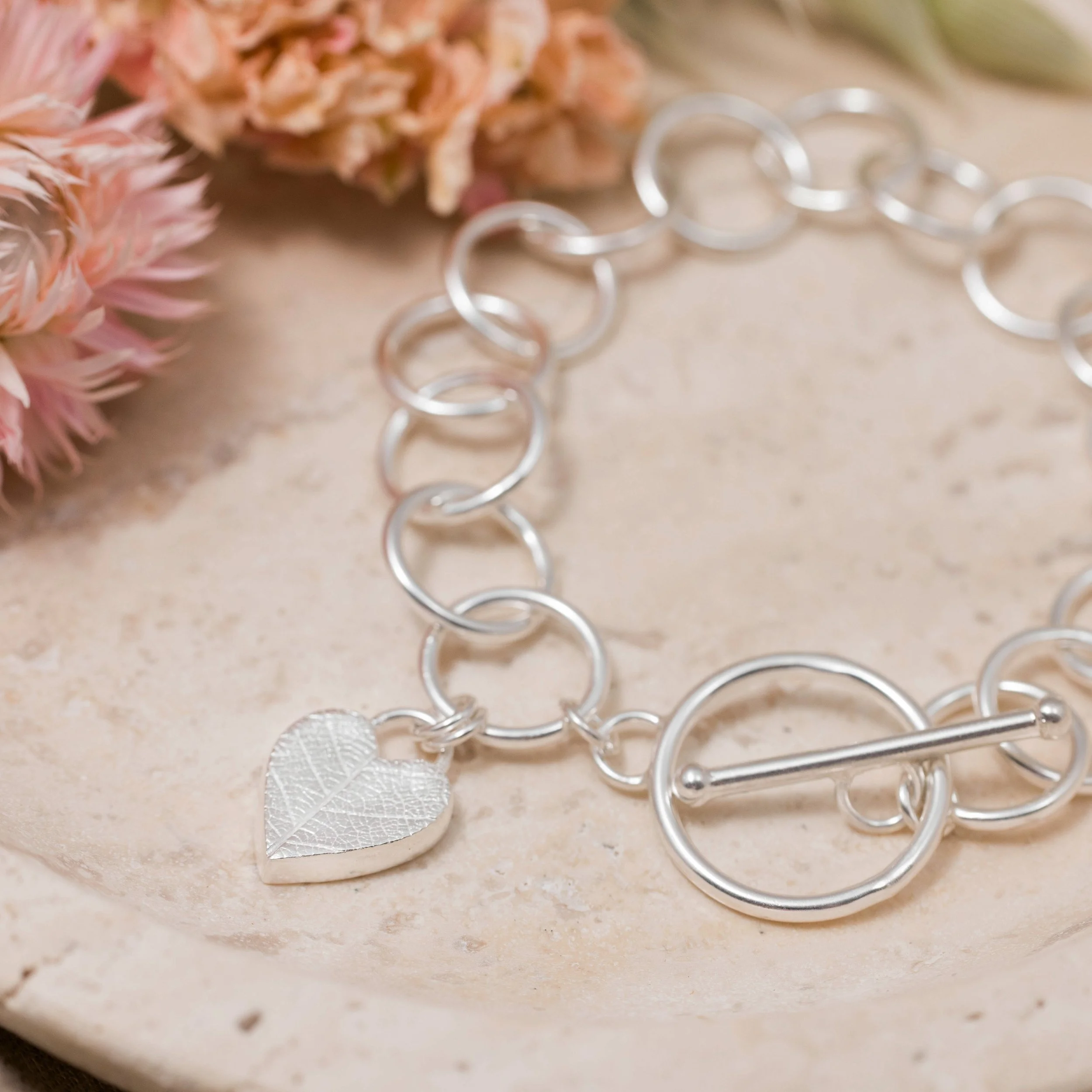 Sterling silver bracelet with a textured heart charm featuring a delicate leaf pattern, finished with a toggle clasp.