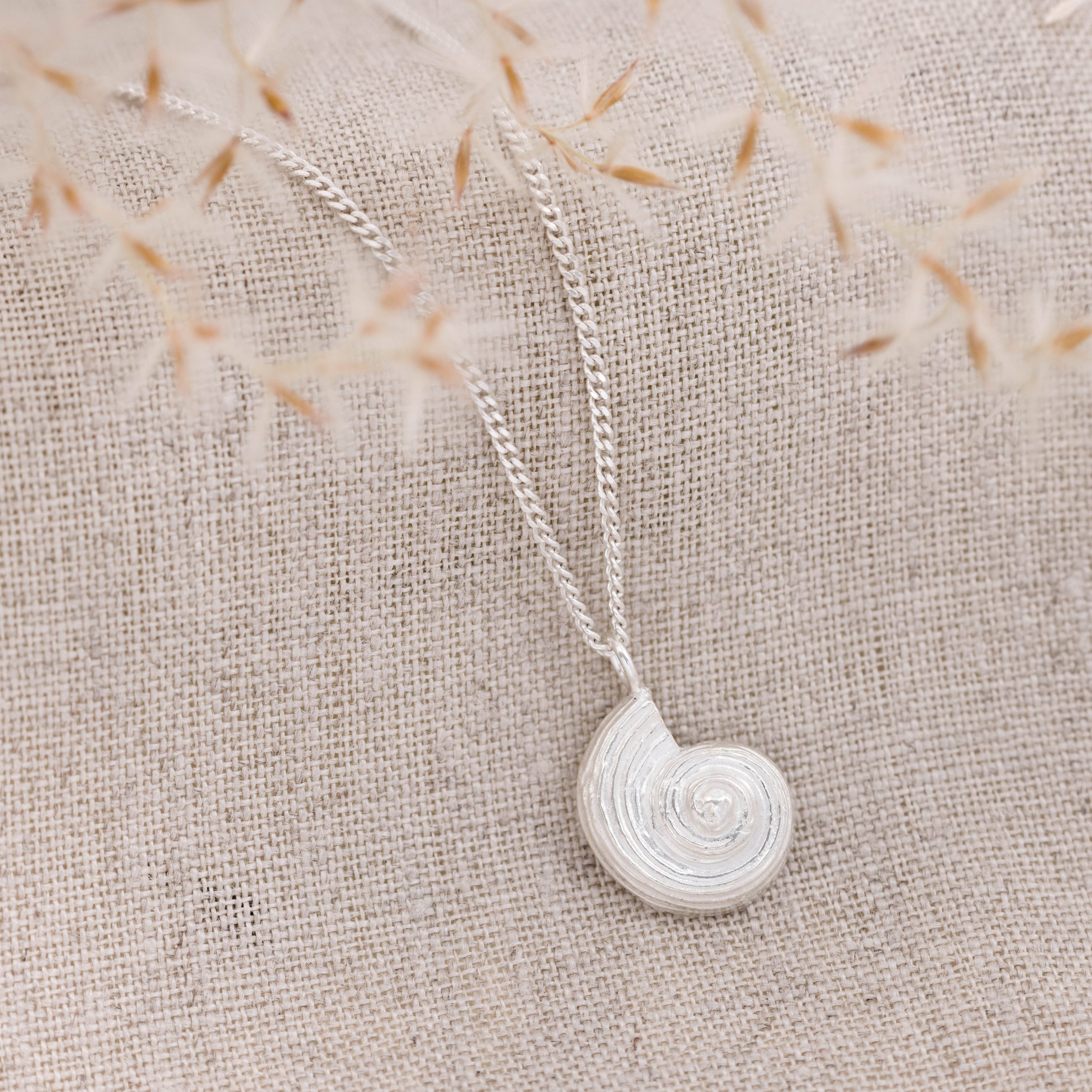 Sterling silver pendant necklace with a detailed fossil ammonite design on a fine chain, inspired by coastal and seaside jewellery.