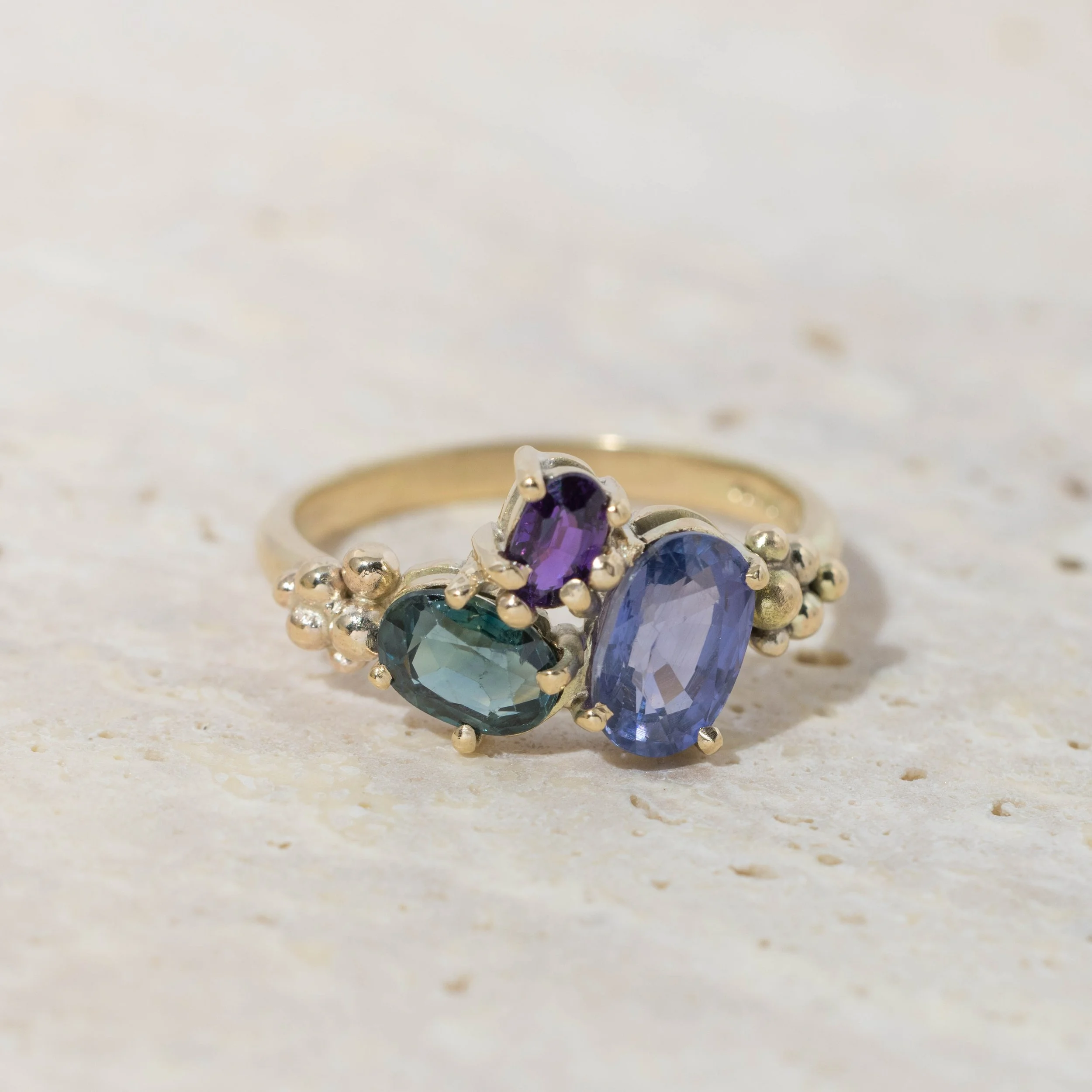 Yellow gold ring with a cluster of sparkling saaphires in teal, deep blue, and purple. Inspired by the colours of the aurora borealis.
