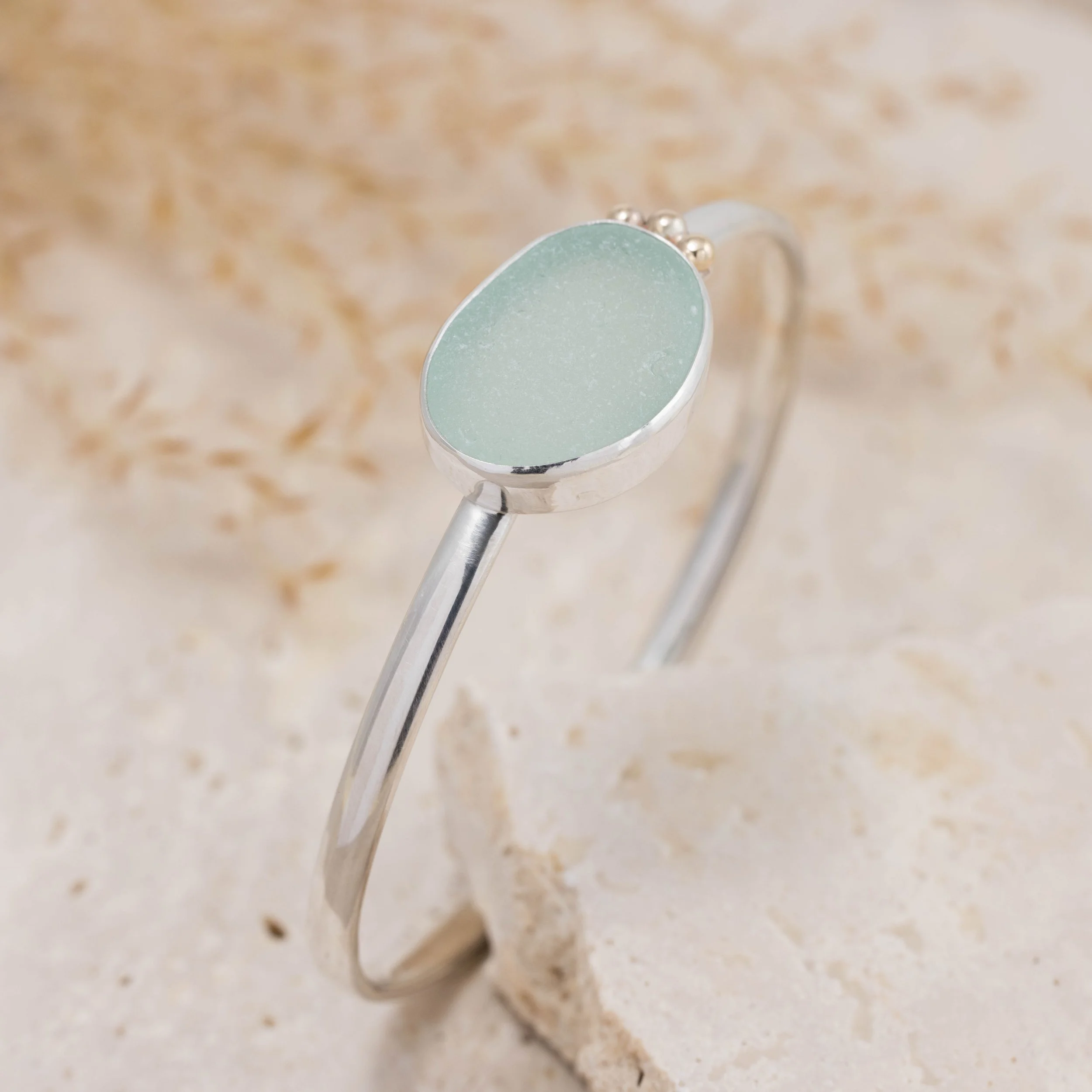 Aquamarine sea glass pebble set with a sterling silver setting and oval band bangle. 9ct gold granulation to highlight. Highly polished finished for this coastal inspired design.