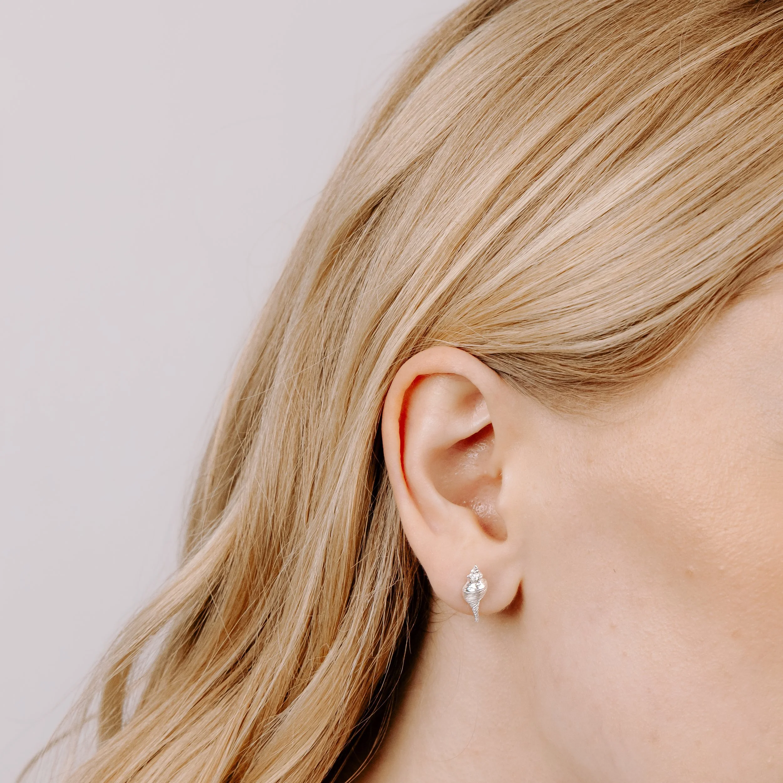 Dainty sterling silver conch shell stud earrings with polished finish, inspired by coastal seashell designs.