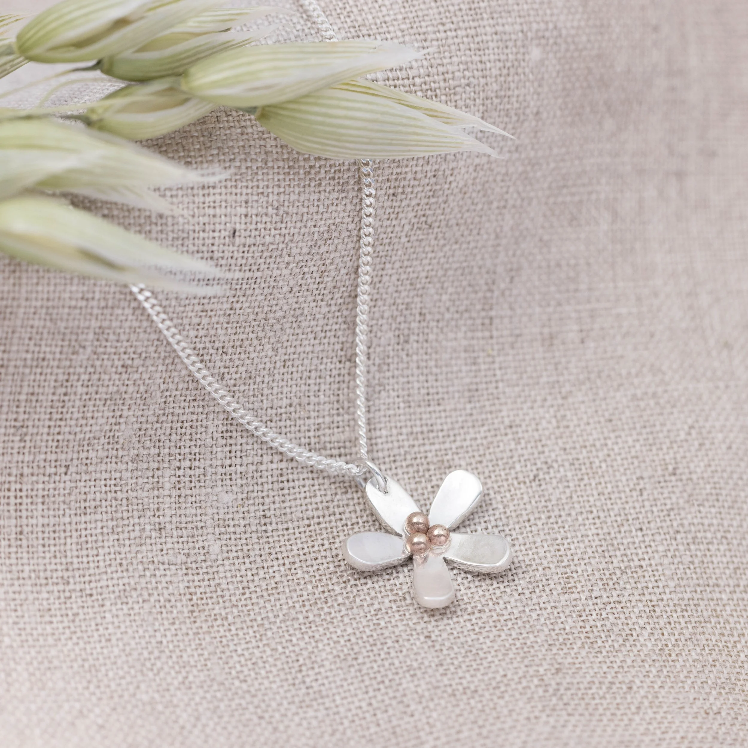 Sterling silver daisy pendant necklace with polished petals and a 9ct gold stamen on a delicate silver chain.