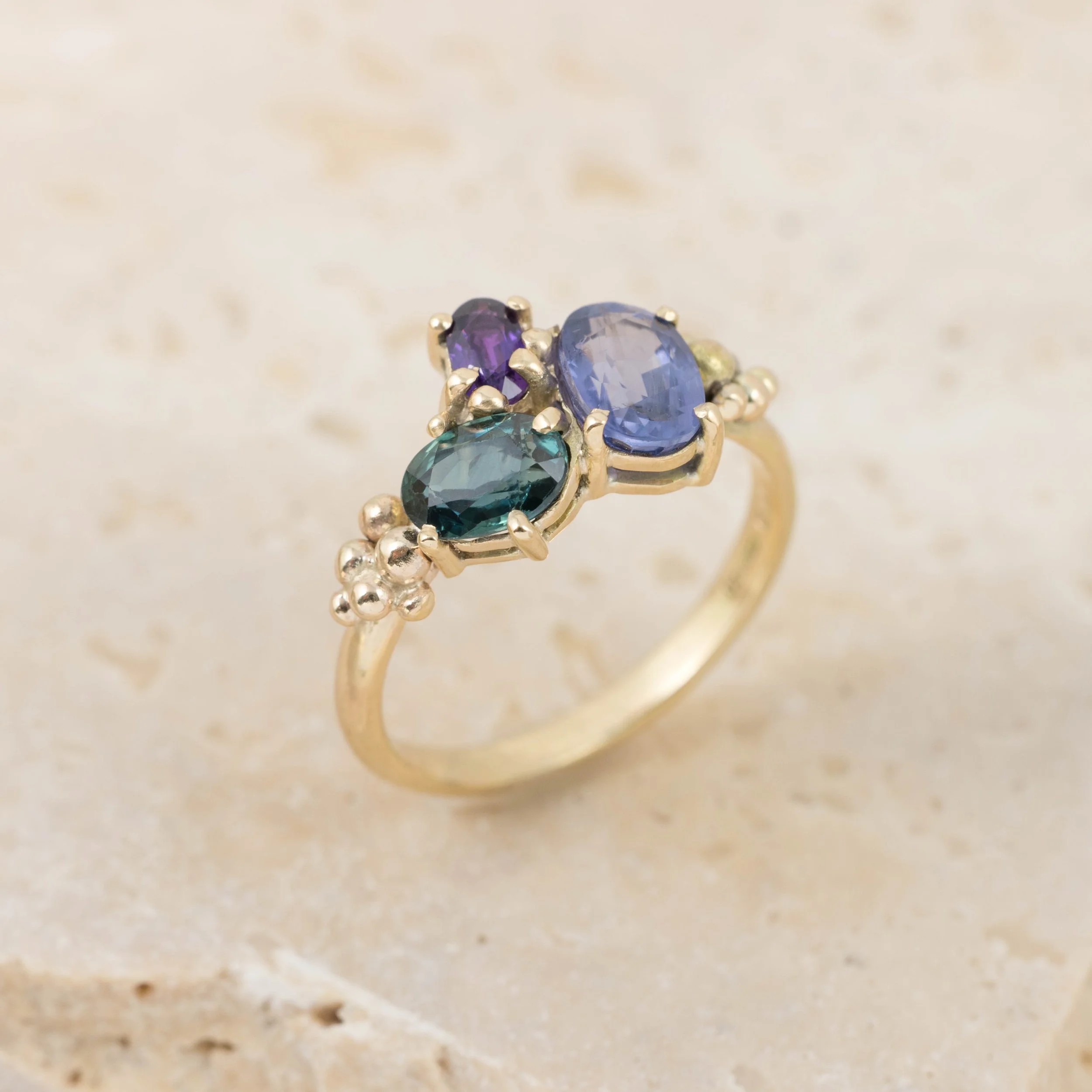 Yellow gold ring with a cluster of sparkling saaphires in teal, deep blue, and purple. Inspired by the colours of the aurora borealis.