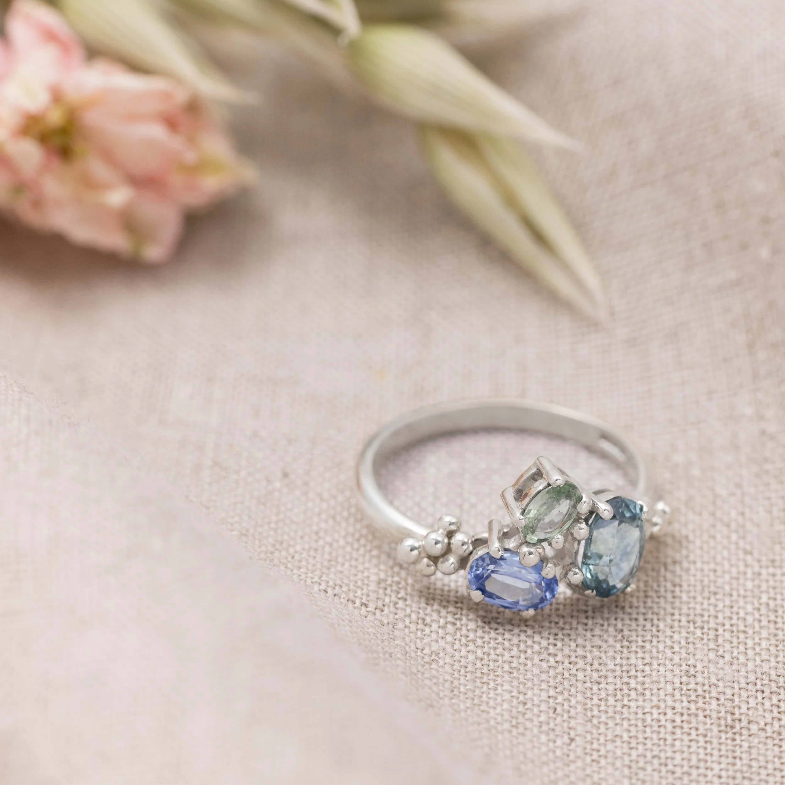 White gold ring with a cluster of oval blue and green sapphires in a seascape-inspired design.