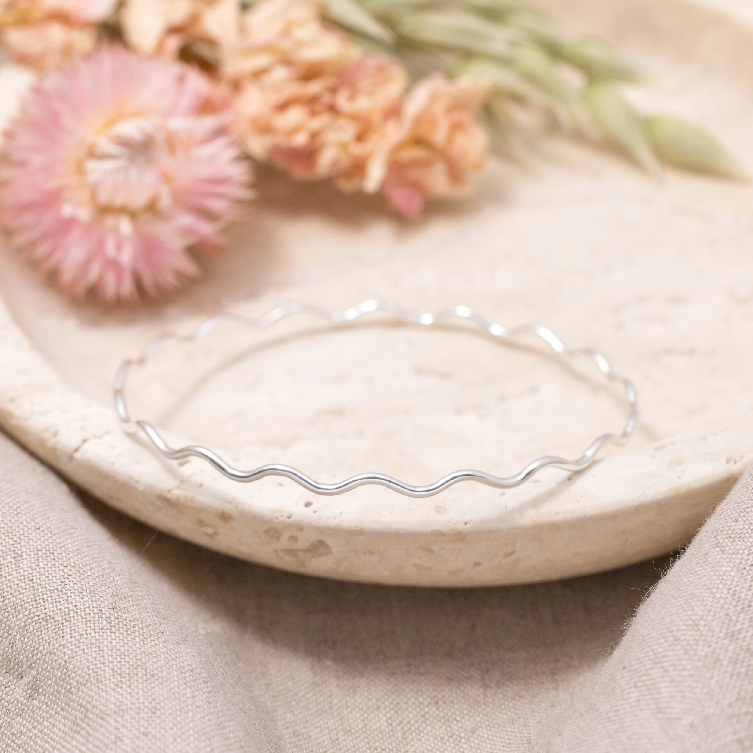 Sterling silver scallop stacking bangle with softly curved edges and polished wave detailing, designed for layering or elegantly worn alone.